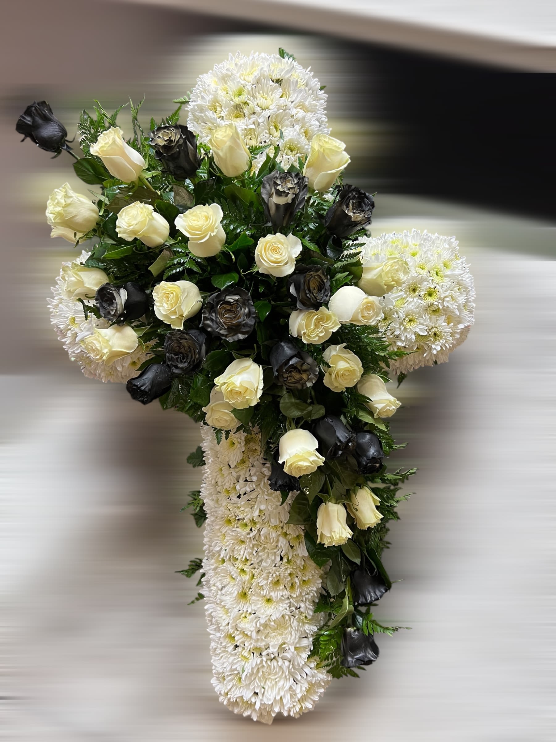 Standing cross of white chrysanthemums with cream and black roses clustered at the center.