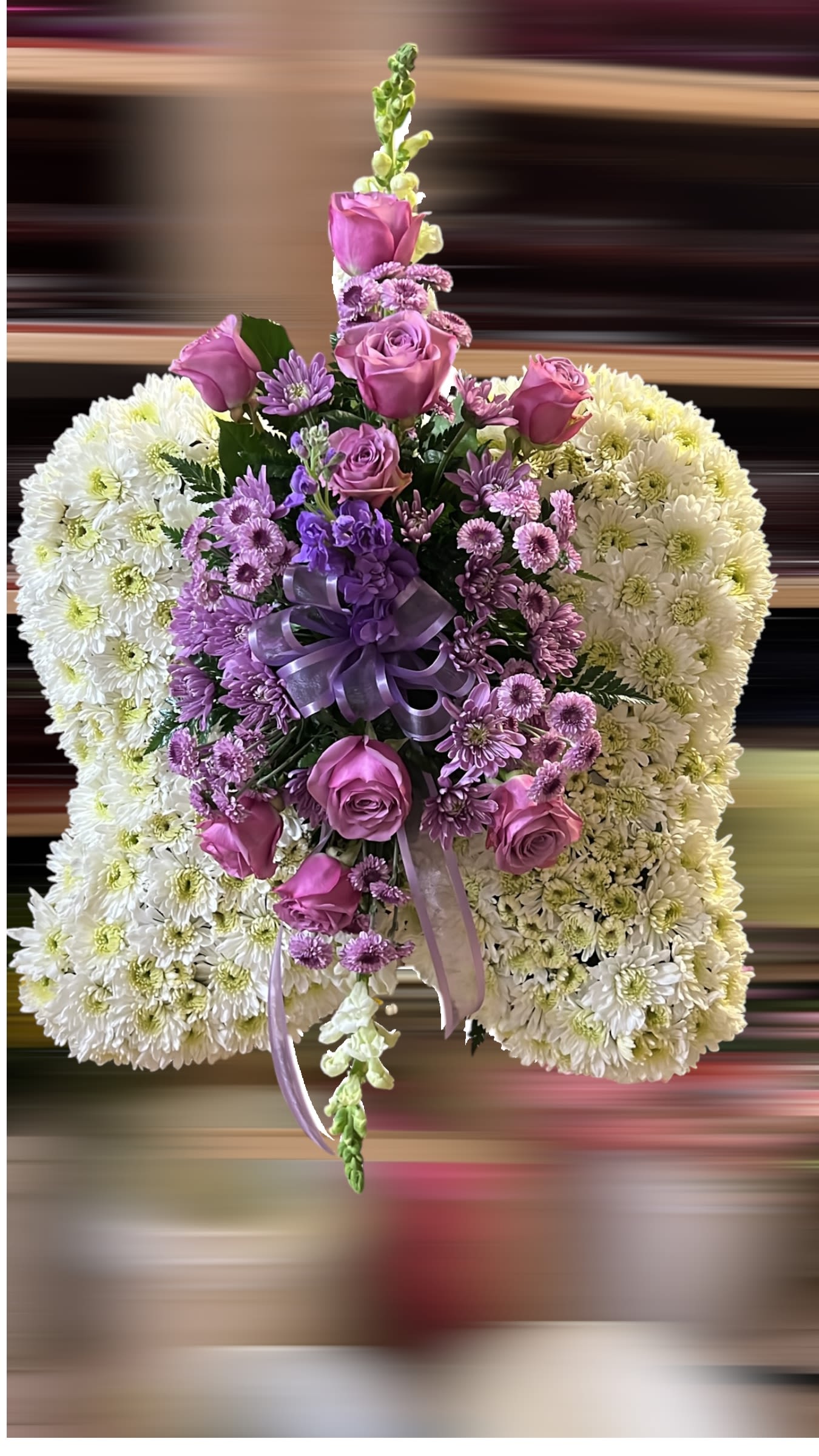 Sympathy pillow of white mums with central spray of lavender roses and daisies, finished with a purple ribbon bow.