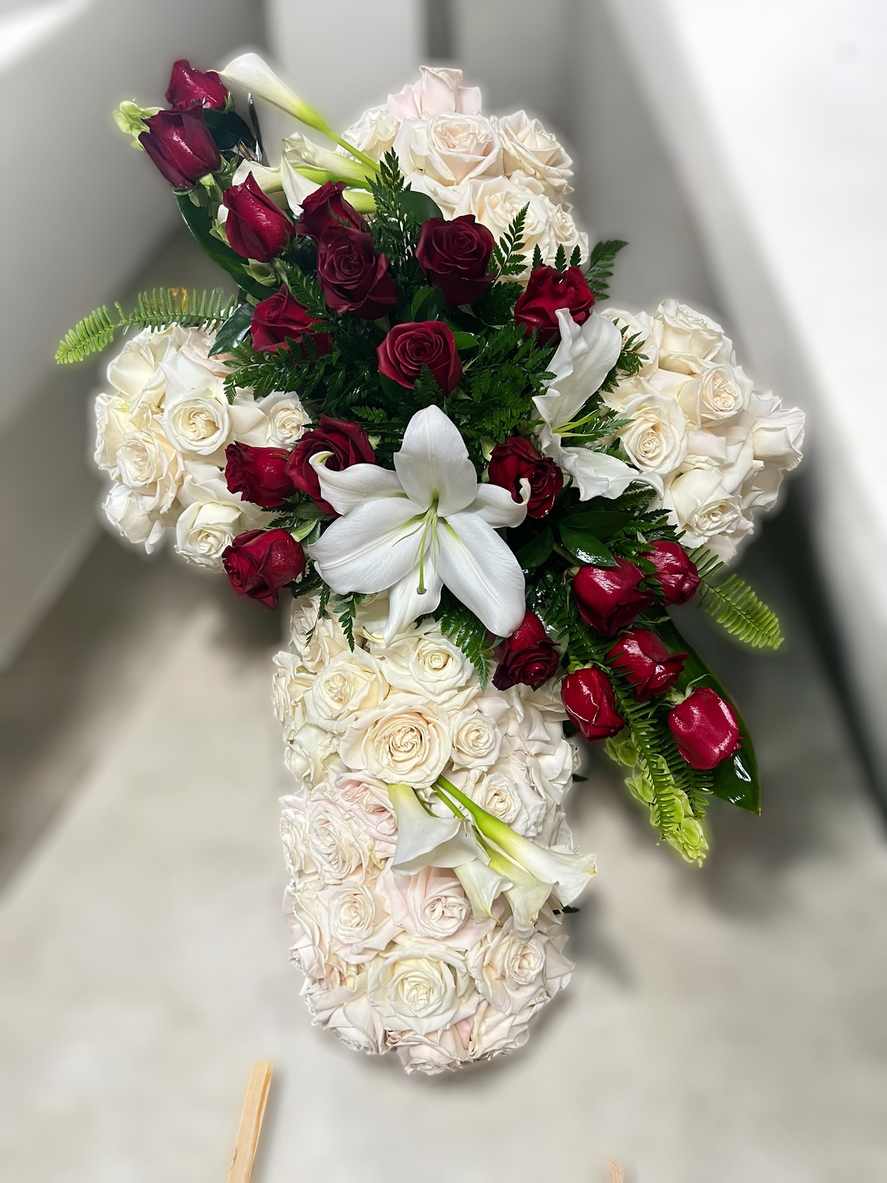 Cross-shaped arrangement of white roses with red roses and white lilies in the center