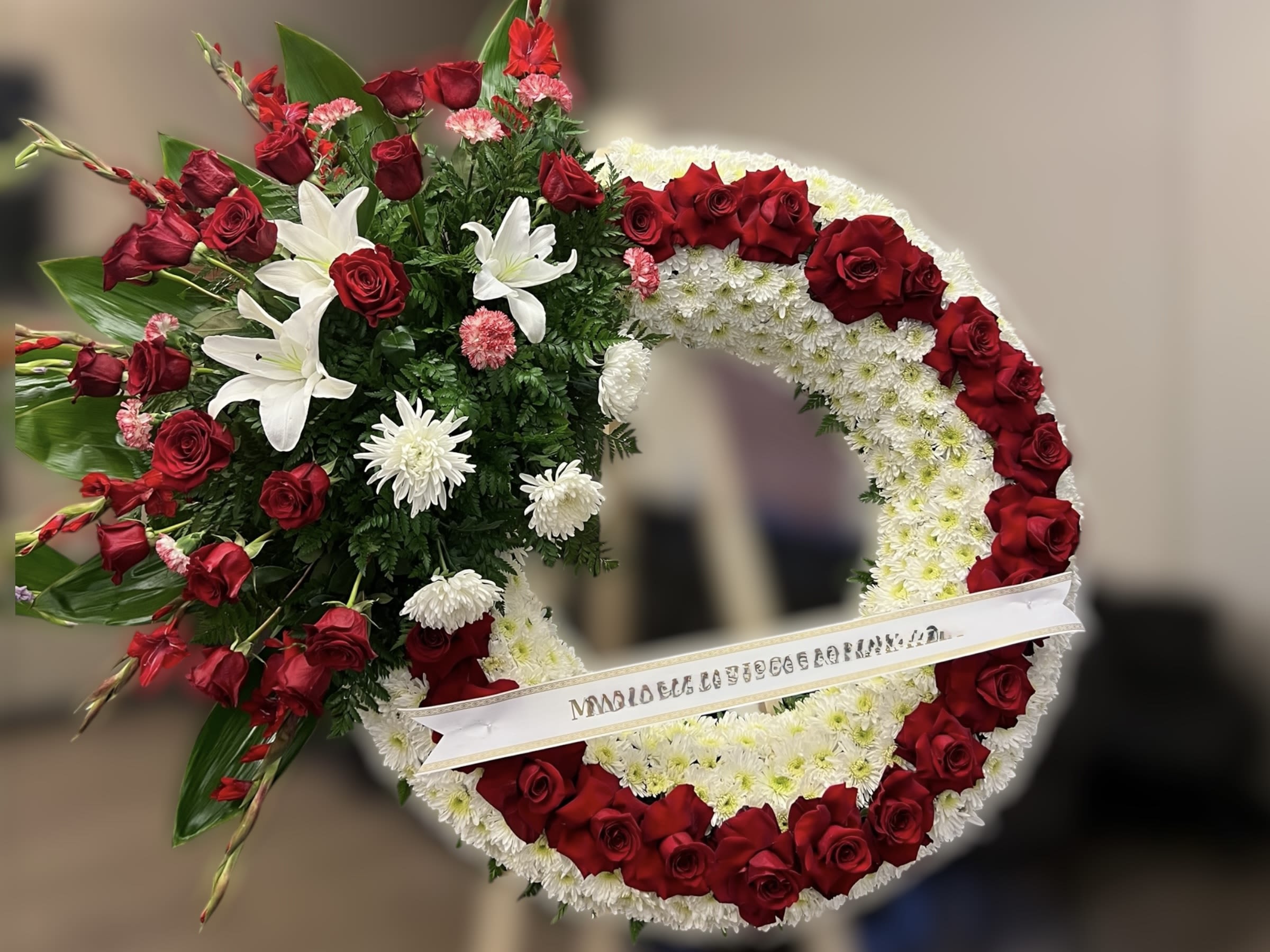 Standing wreath of red roses and white flowers with a side spray on a white ribbon banner.