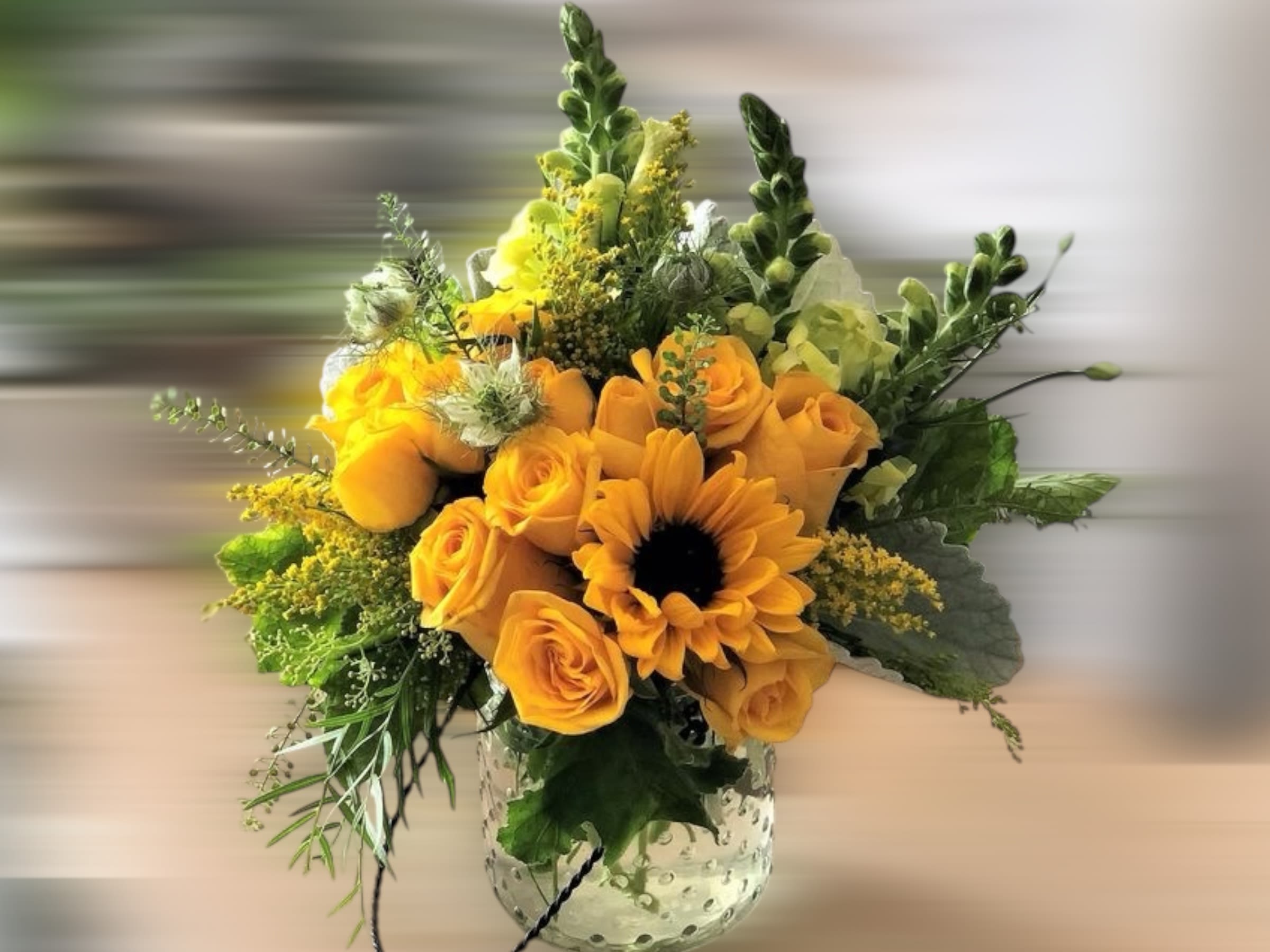 Yellow roses and a sunflower arranged with accent blooms in a clear textured glass vase