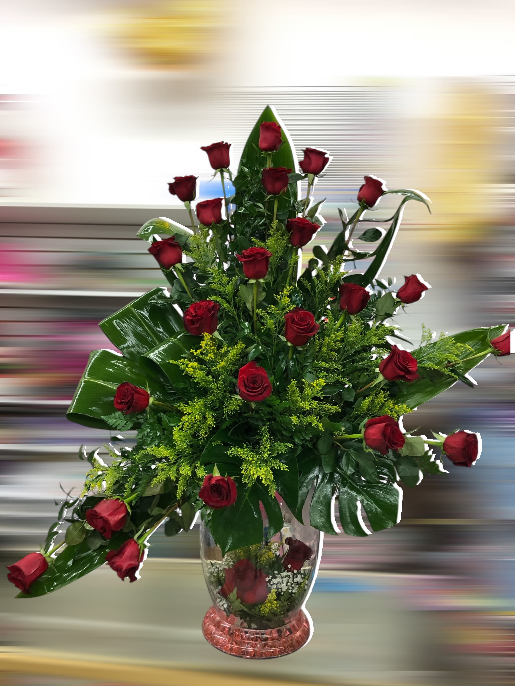 Tall arrangement of red roses with large tropical leaves in a clear glass vase