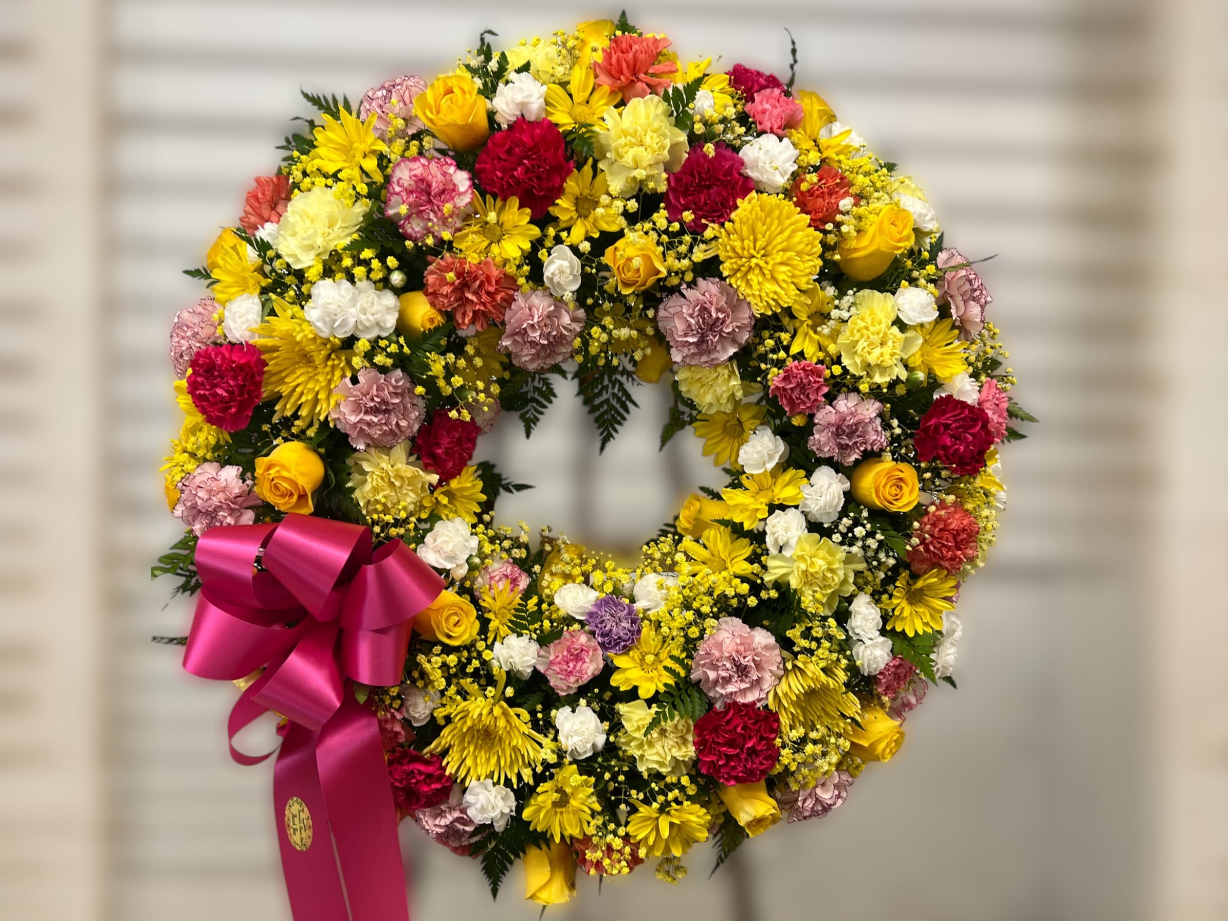 Bright standing wreath of yellow, pink, white, and red flowers with a hot pink ribbon bow