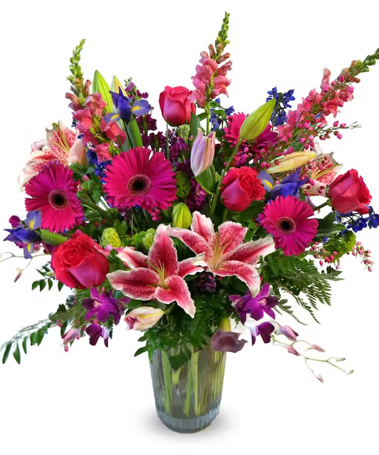 Tall mixed bouquet of pink lilies, roses, gerbera daisies and purple flowers in a clear glass vase