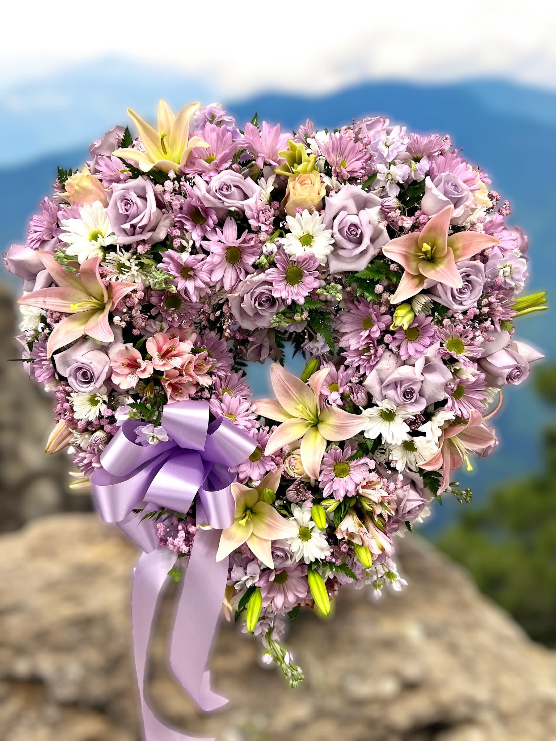 Heart-shaped wreath of pink and lavender flowers with a purple ribbon bow