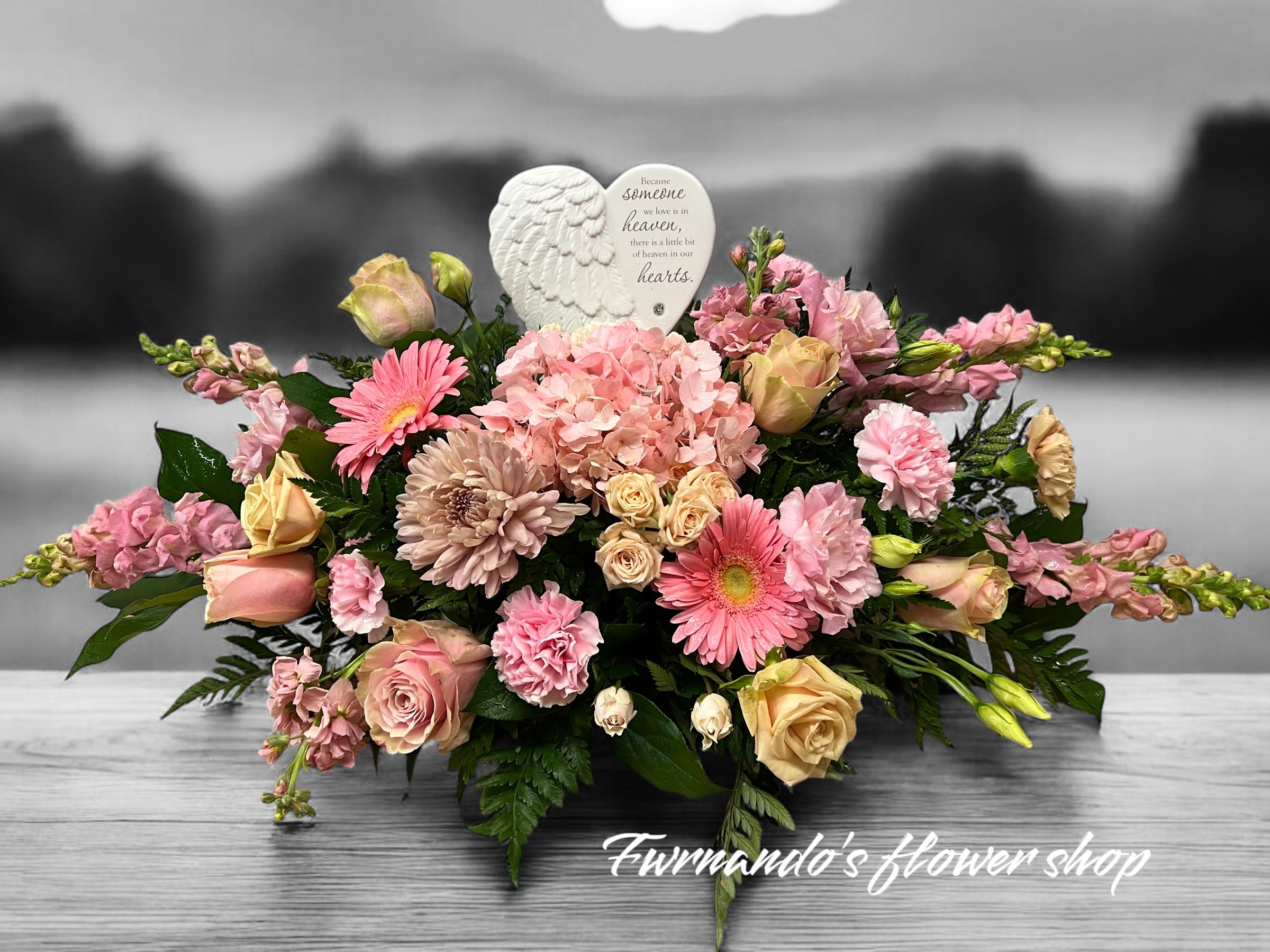 Low pink and peach sympathy arrangement with roses, gerberas, hydrangeas and a heart-shaped angel wings plaque.