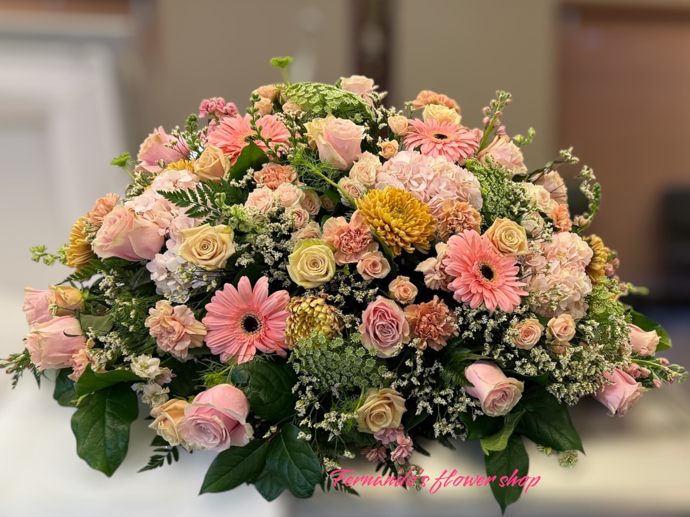 Low casket-style spray of pink and peach roses, gerberas, carnations, and mums with white filler flowers