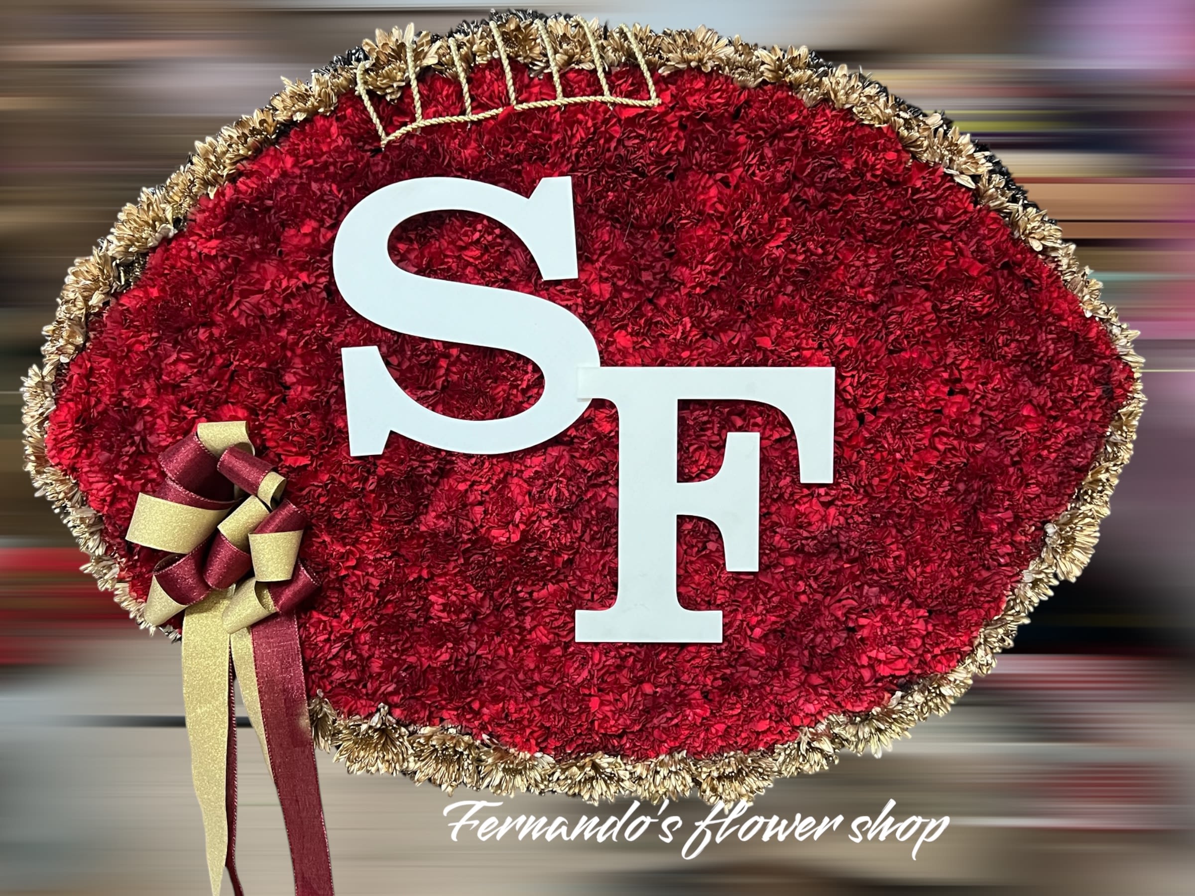Football-shaped red carnation floral display with white SF letters and gold and burgundy ribbon.