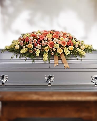 Peach and yellow casket spray of roses and mixed blooms with ribbon on a silver casket