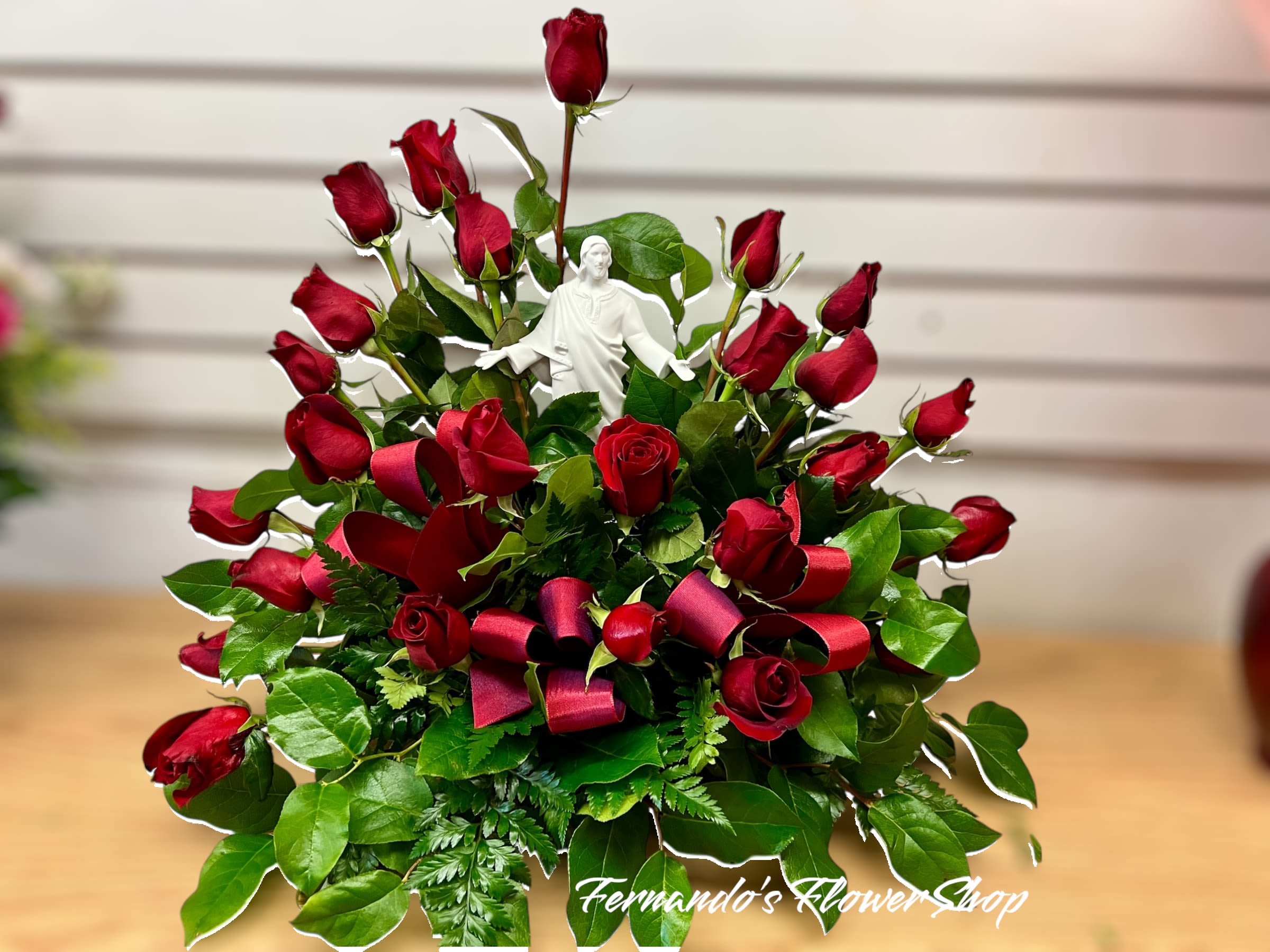 Fan-shaped arrangement of red roses with a white Jesus figurine and red ribbon loops
