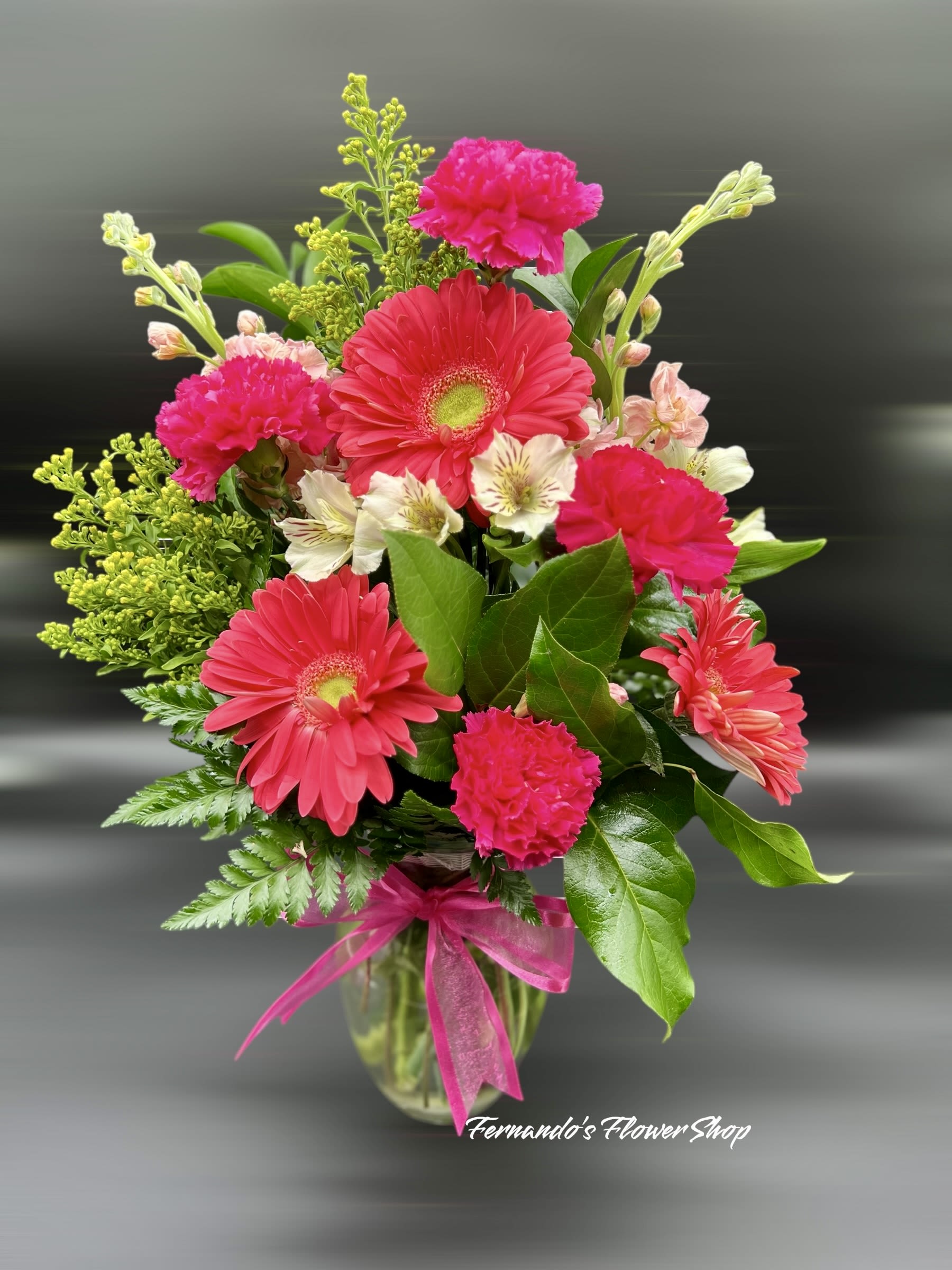 Bright pink gerbera daisies, carnations, and light alstroemeria in a clear vase with pink bow