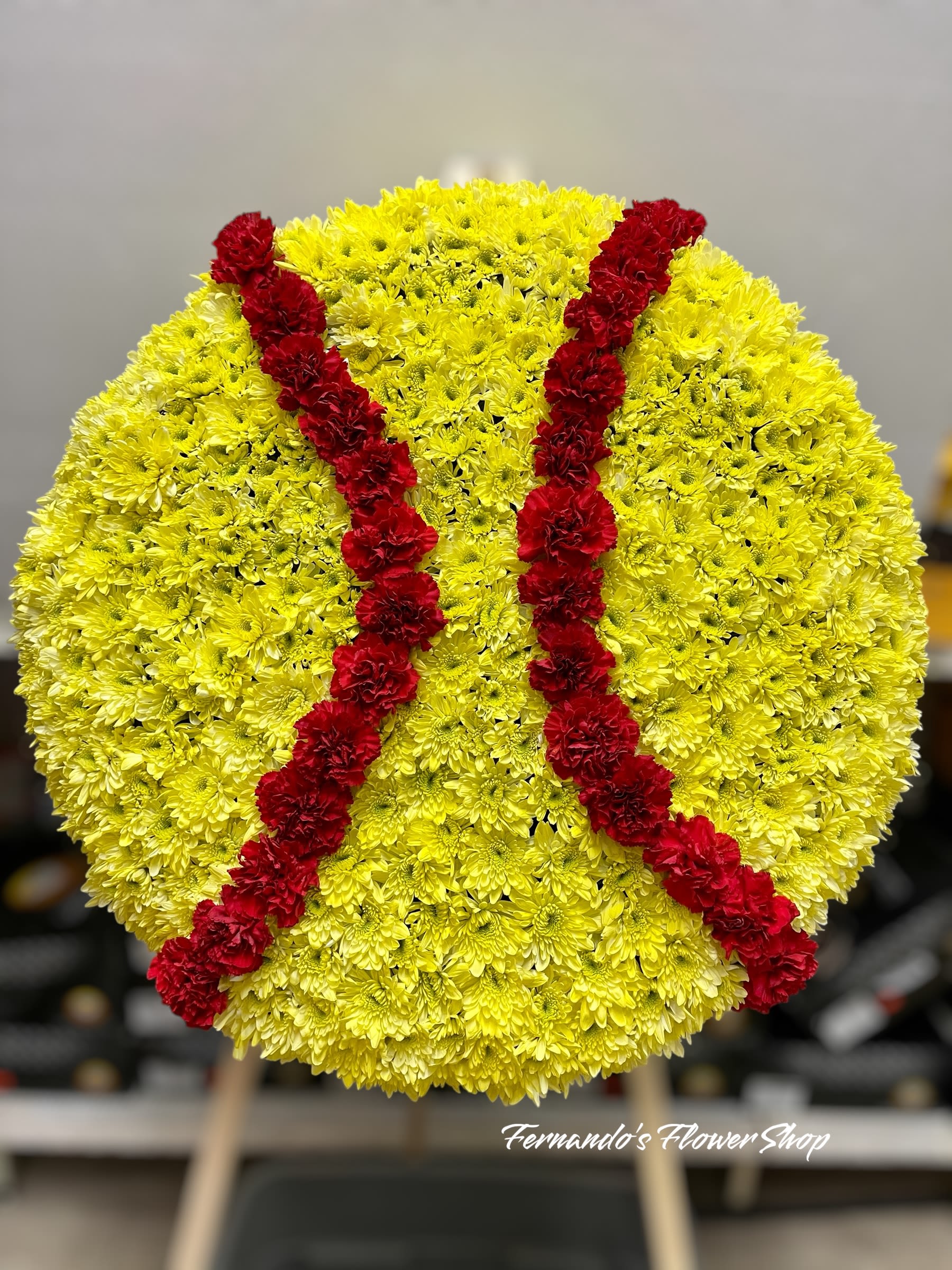 Round yellow floral standing spray shaped like a softball with red stitching lines