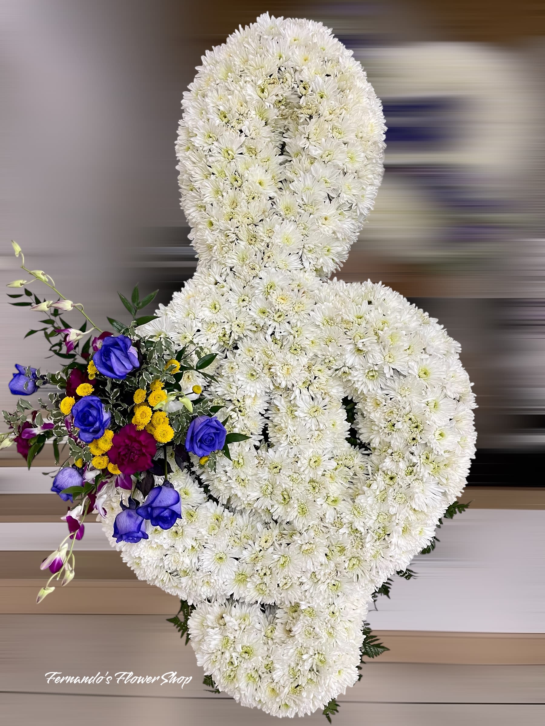 Standing white chrysanthemum ribbon arrangement with blue roses and mixed accent flowers.