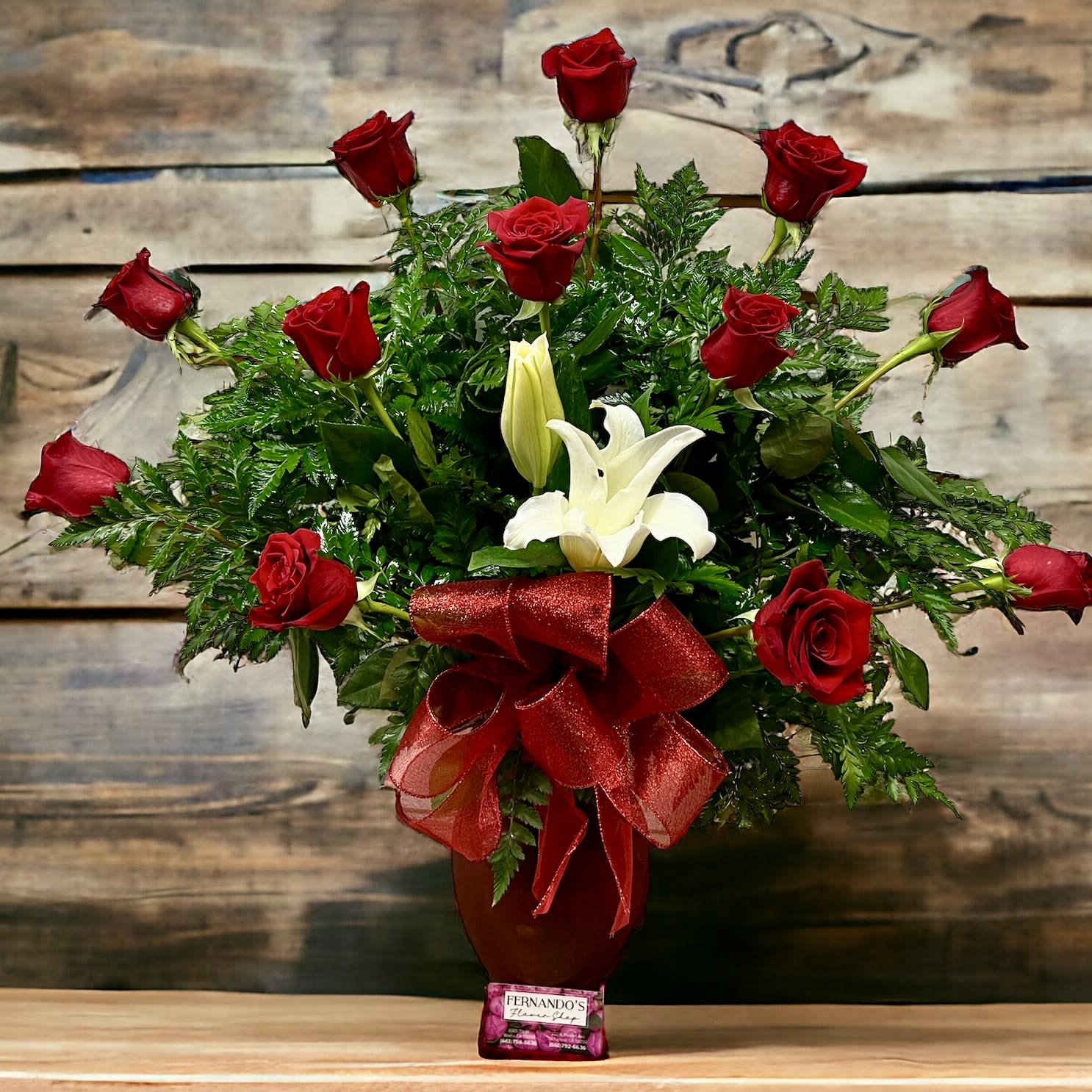 Tall arrangement of red roses and white lilies in a red vase with red bow and chocolates