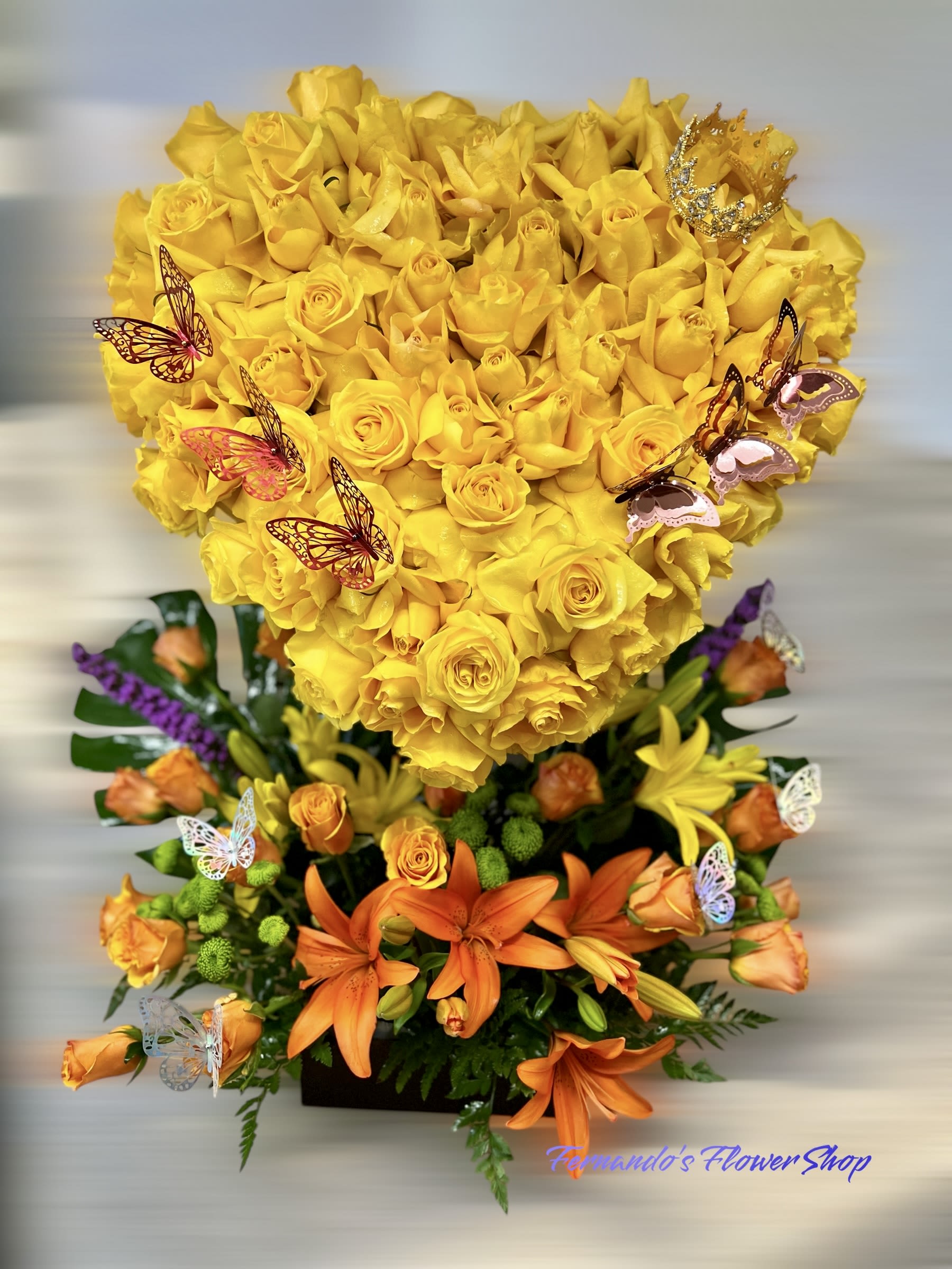 Tall arrangement with a yellow rose heart over orange lilies and roses with butterfly accents