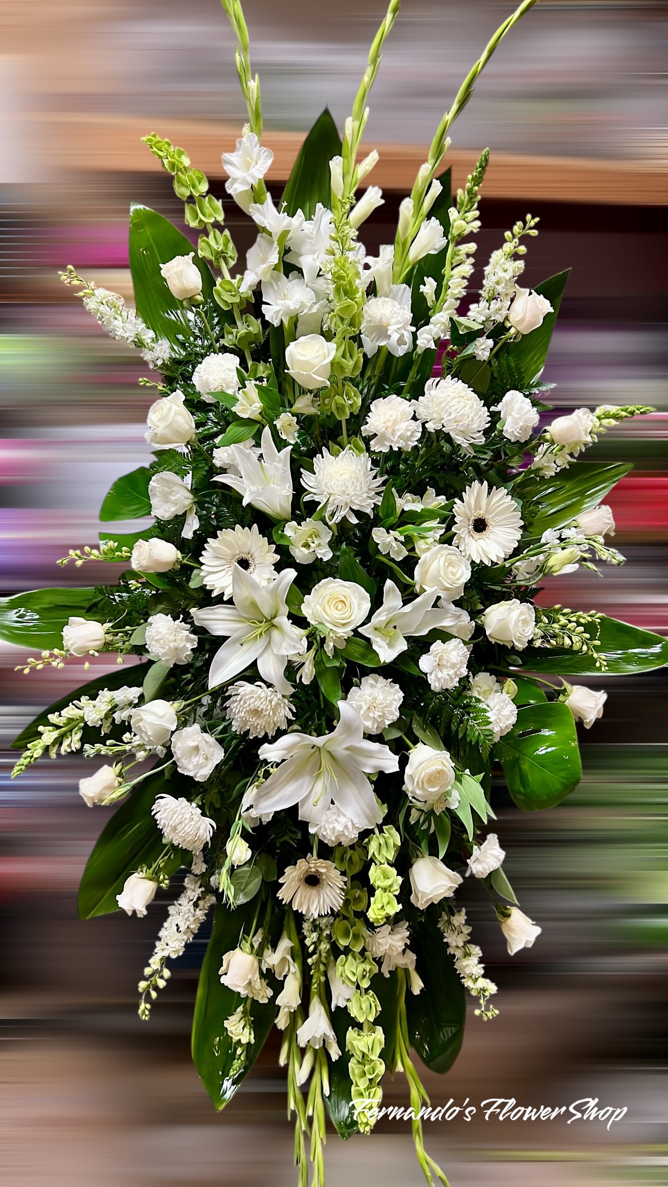 Tall standing spray of white lilies, roses, carnations, and other blooms in an elongated design