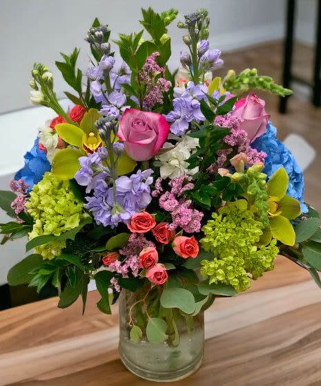 Colorful mixed bouquet with pink roses, orchids, hydrangeas and stock in a clear glass jar vase