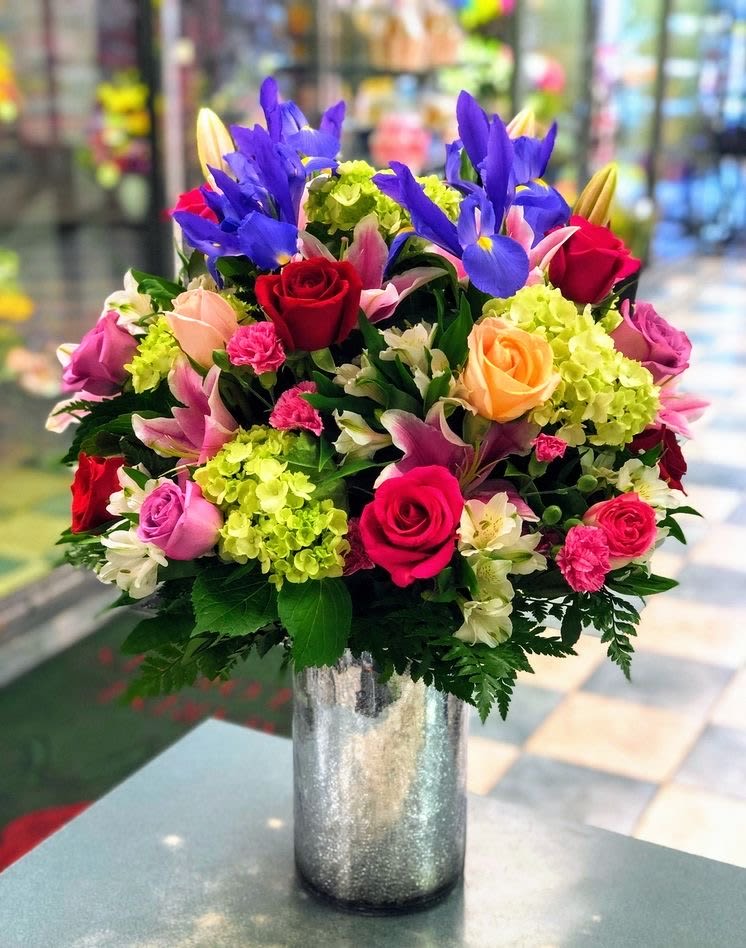 Tall mixed bouquet of roses, lilies, irises, and hydrangeas in a silver glass vase