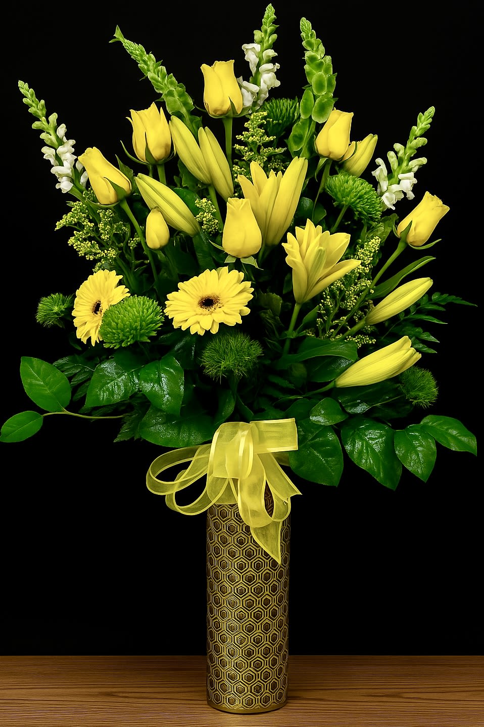 Tall yellow and green floral arrangement with lilies, roses, and daisies in a patterned cylinder vase with bow
