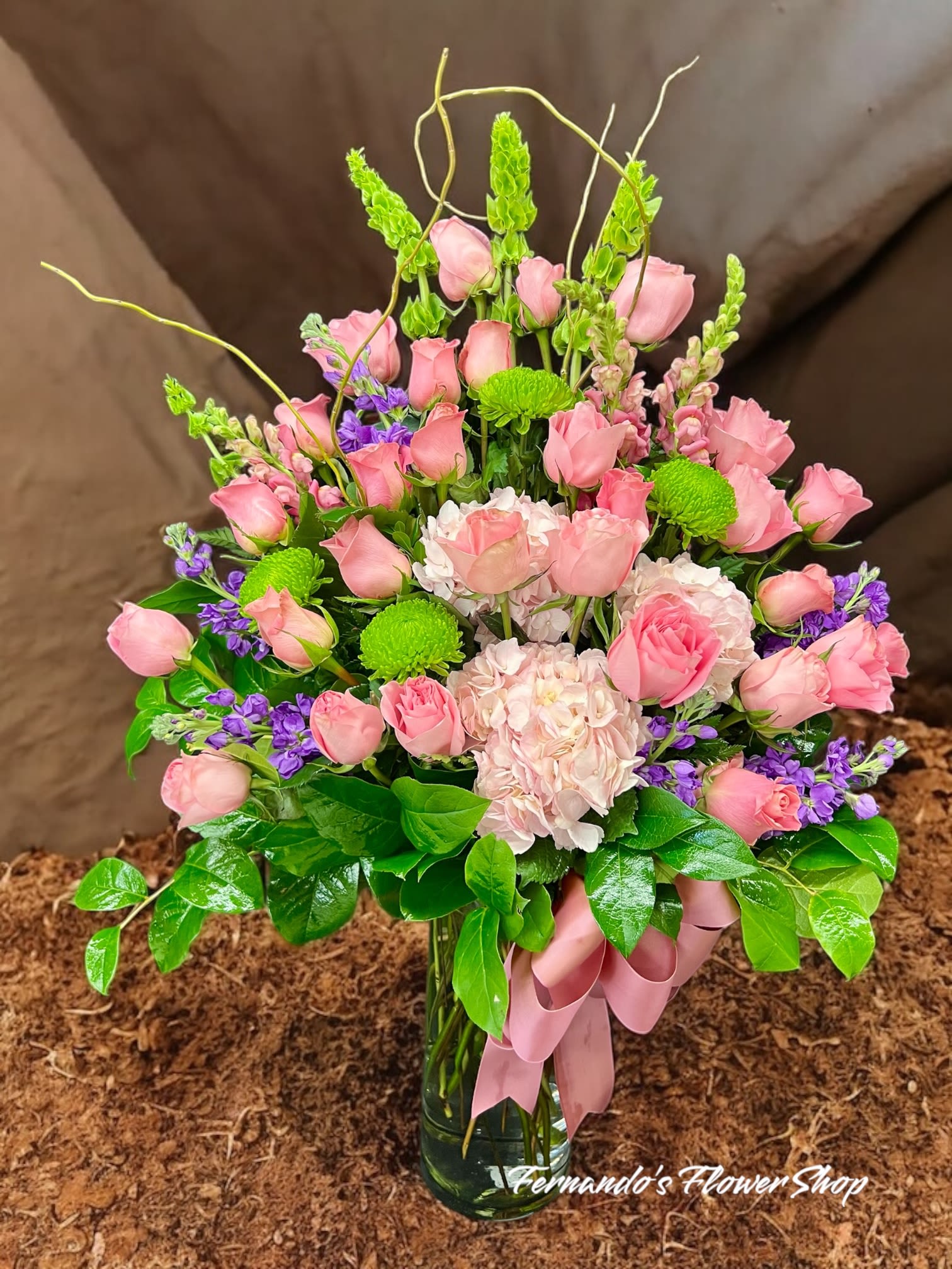 Tall pink rose and hydrangea arrangement with green mums and bells of Ireland in a glass vase