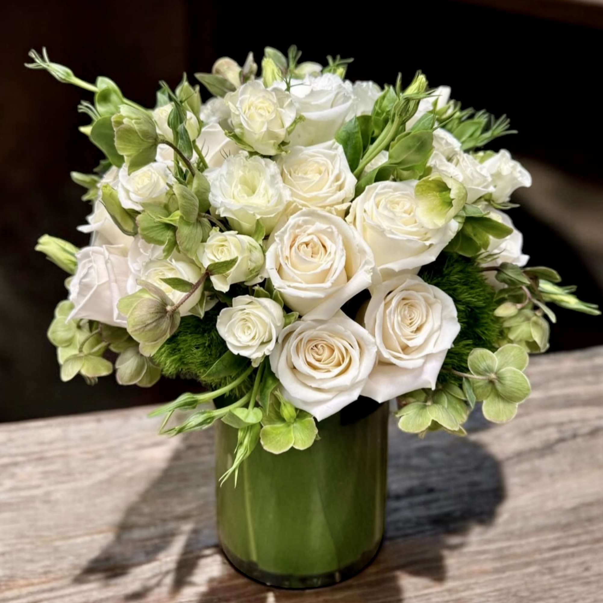 Compact arrangement of white roses and green blooms in a green glass cylinder vase