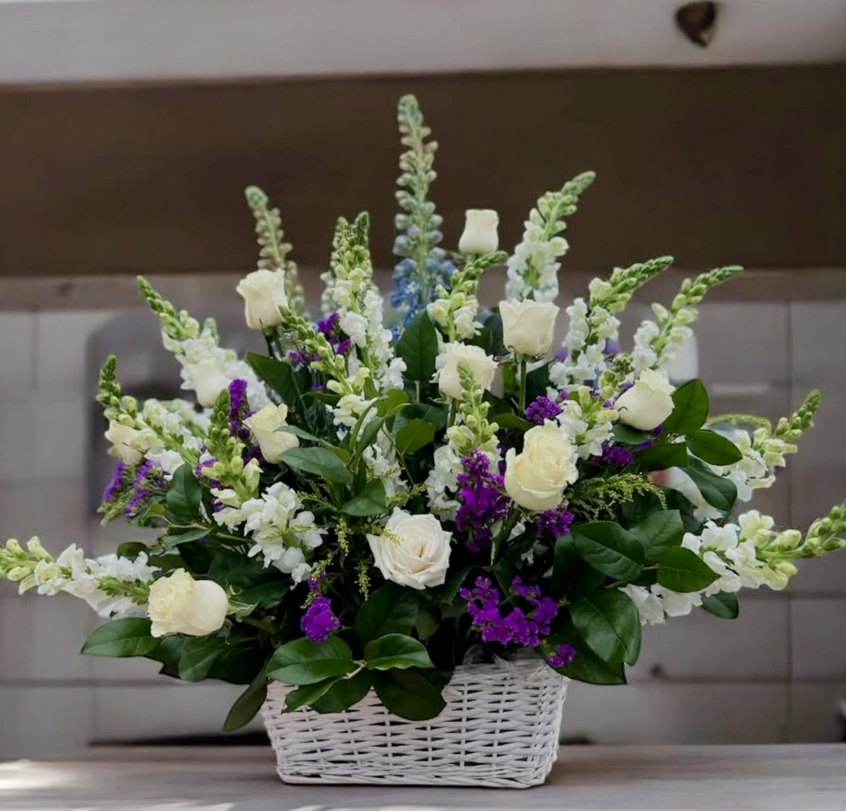 Tall basket arrangement of white roses and snapdragons with purple accents