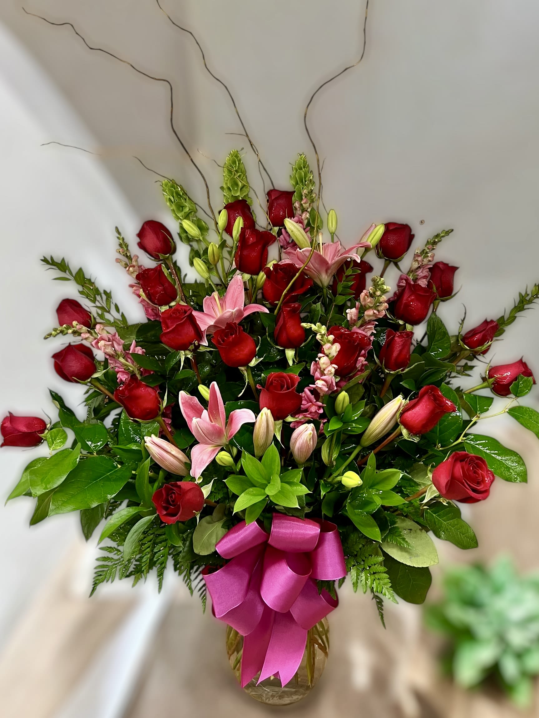 Tall arrangement of red roses and pink lilies in a glass vase with a bright pink bow