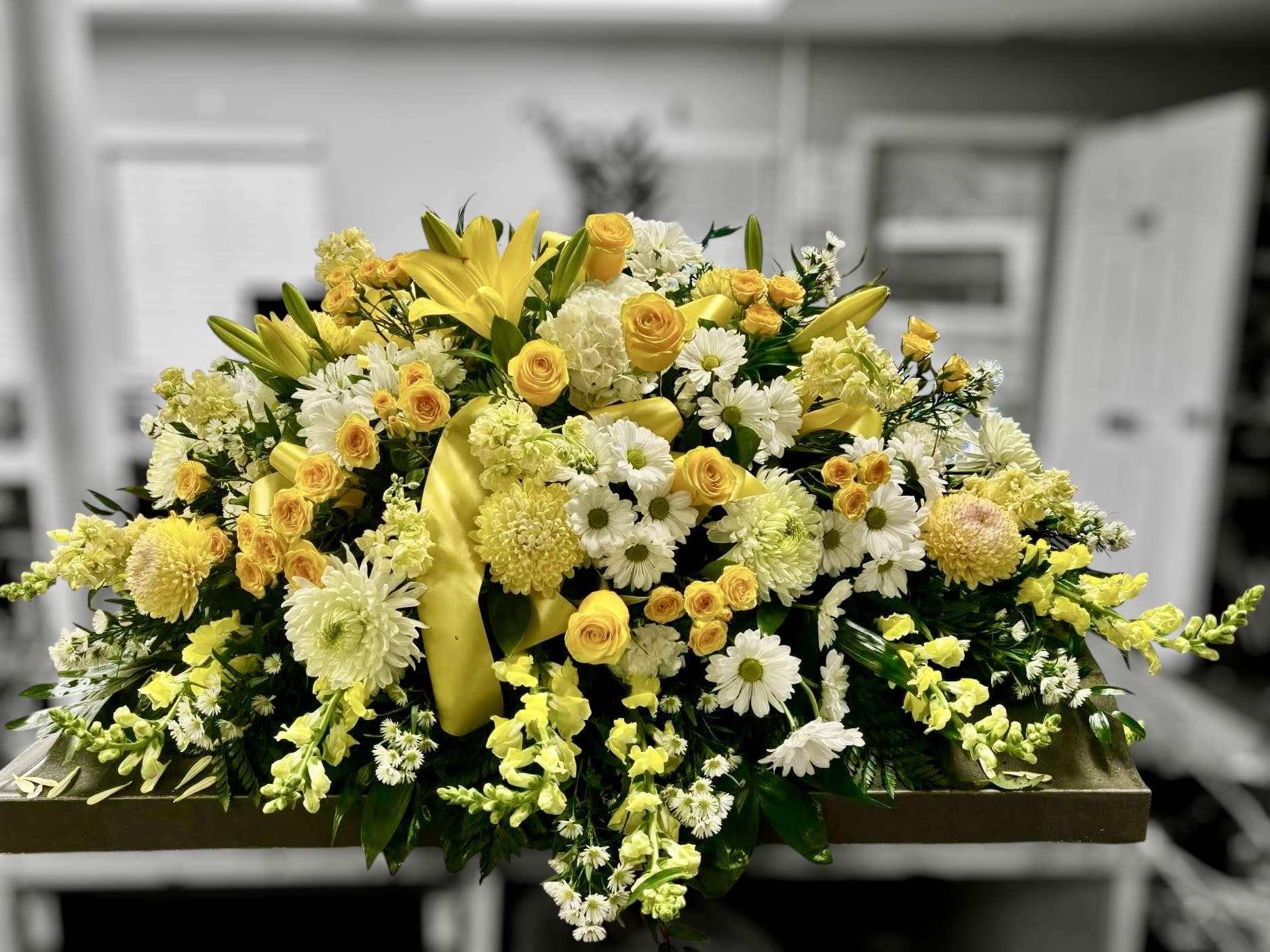 Large yellow and white casket spray with lilies, roses, daisies, and mums on a low rectangular base