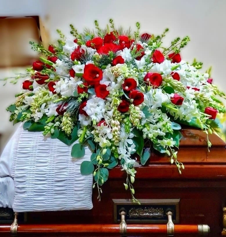 Red and white casket spray of roses and mixed white flowers on a wooden casket