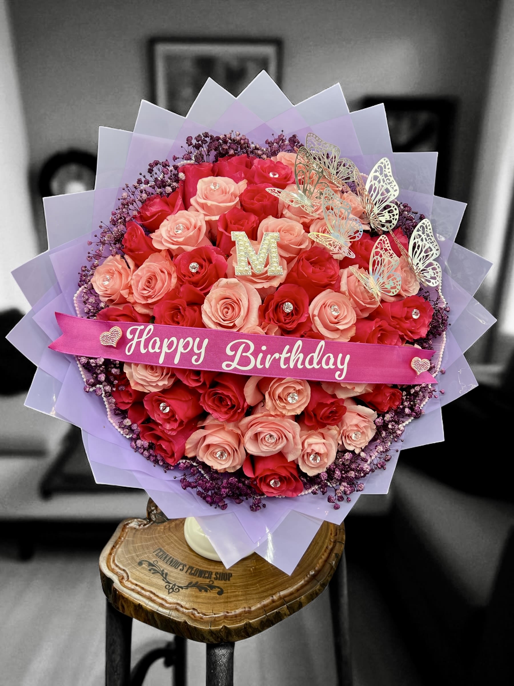 Round bouquet of red and peach roses with birthday ribbon and butterflies wrapped in lavender paper