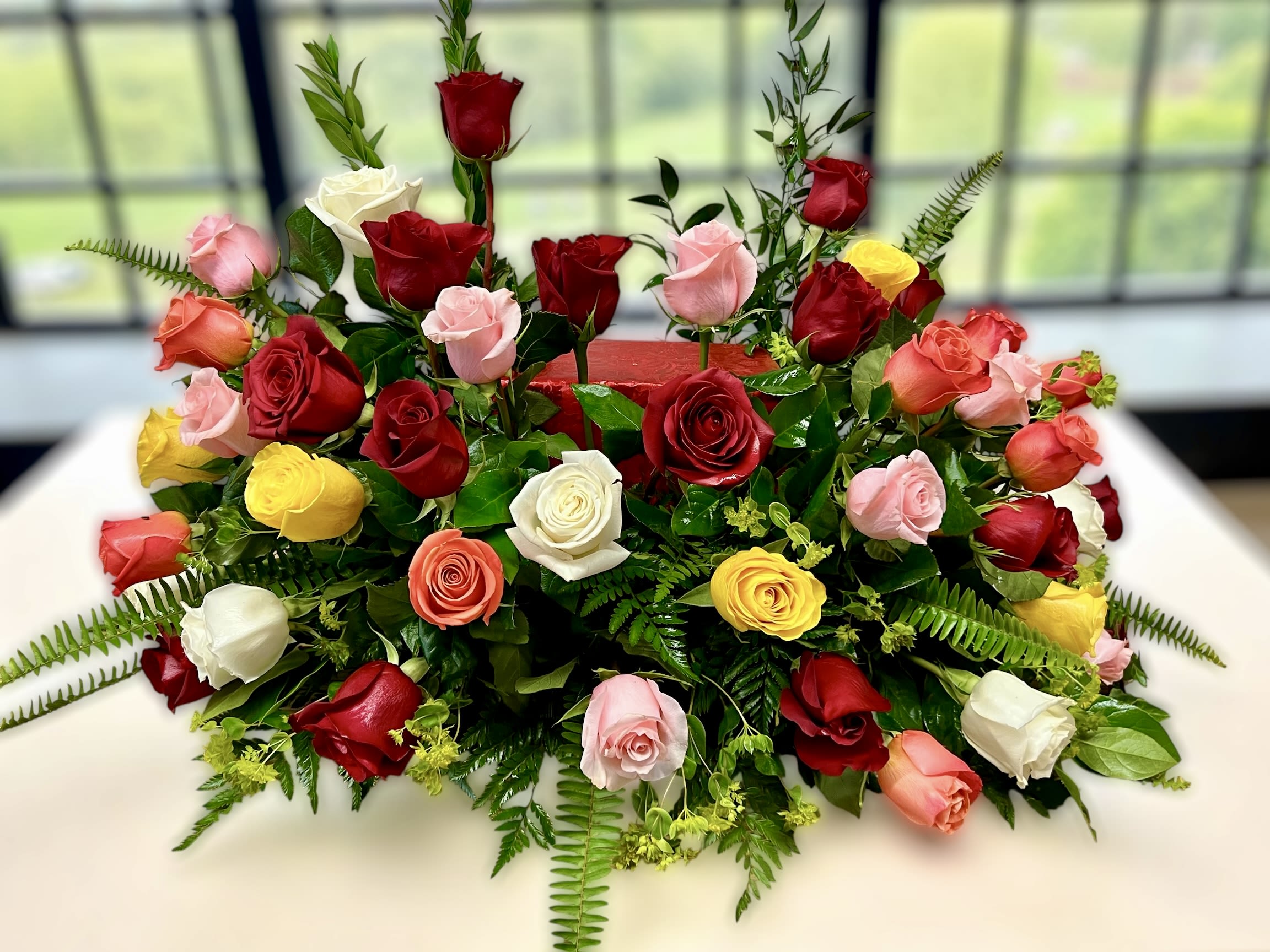 Low centerpiece of red, pink, yellow, and white roses arranged in a long, lush spray