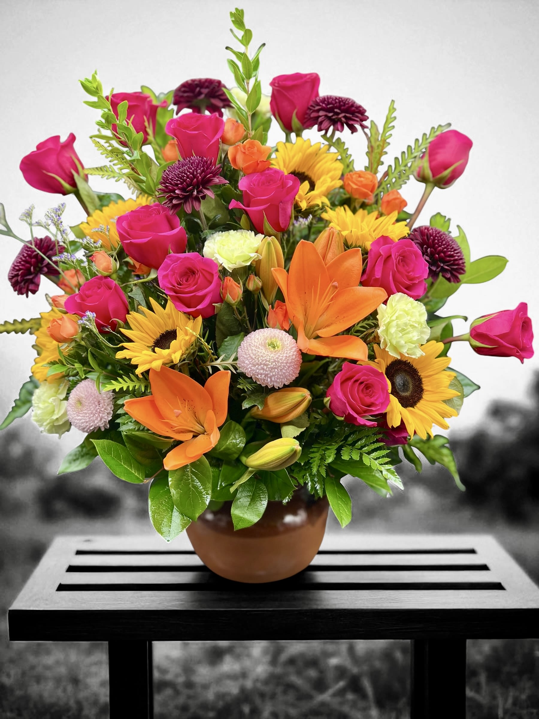 Colorful arrangement of pink roses, orange lilies, and yellow sunflowers in a terracotta pot