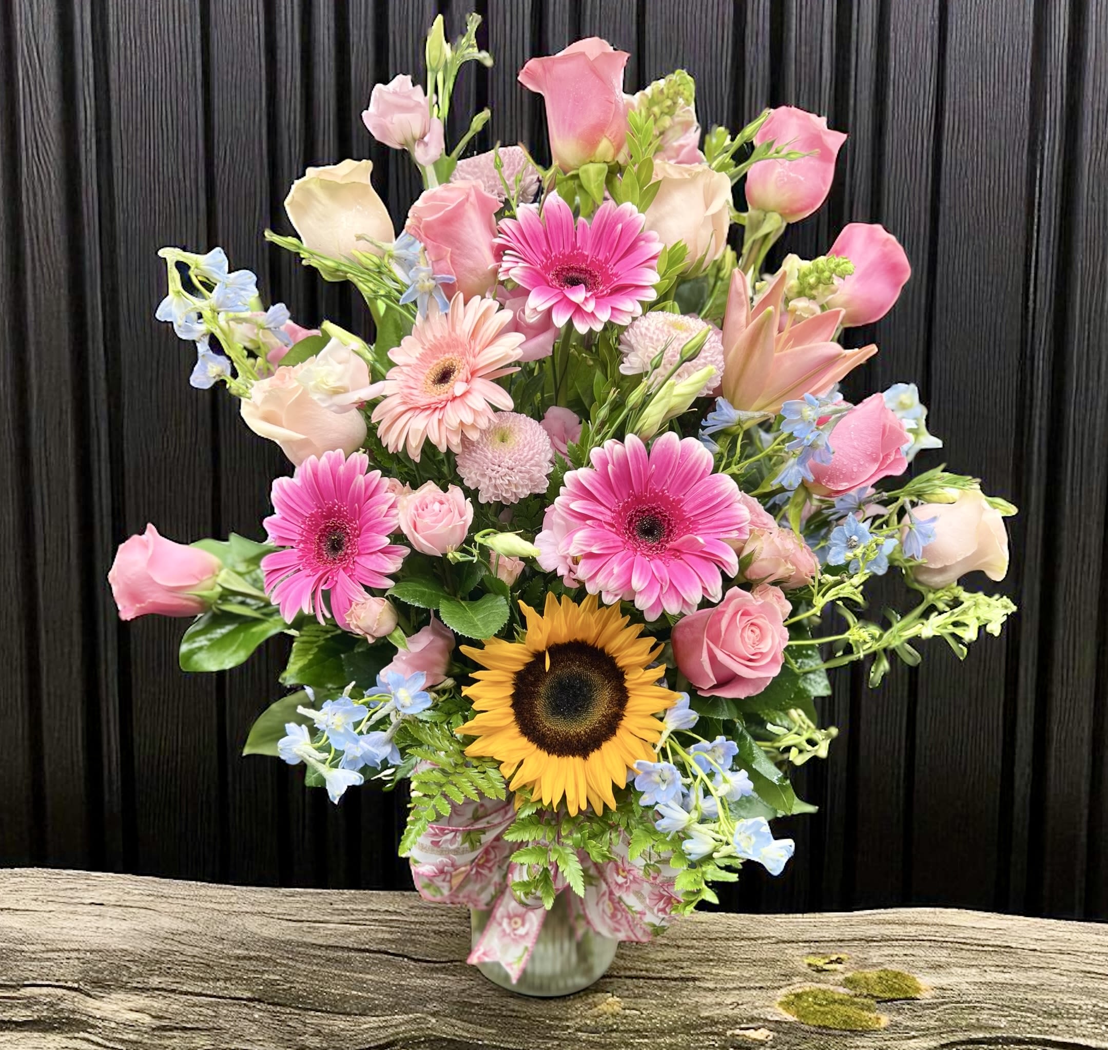 Tall mixed bouquet of pink roses and gerbera daisies with a sunflower in a glass vase