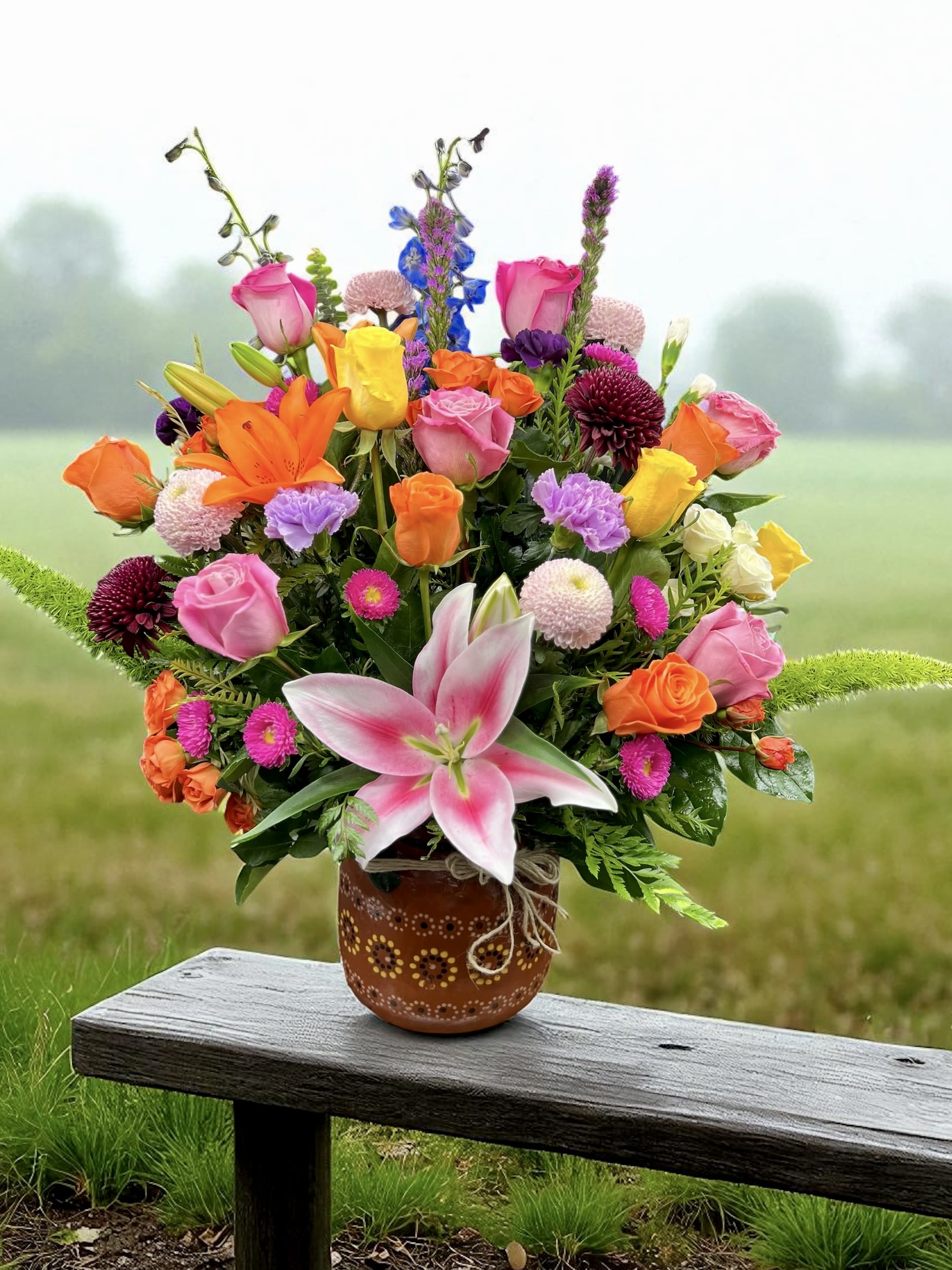 Colorful mixed bouquet of roses, lilies, and other blooms in a brown patterned ceramic pot.