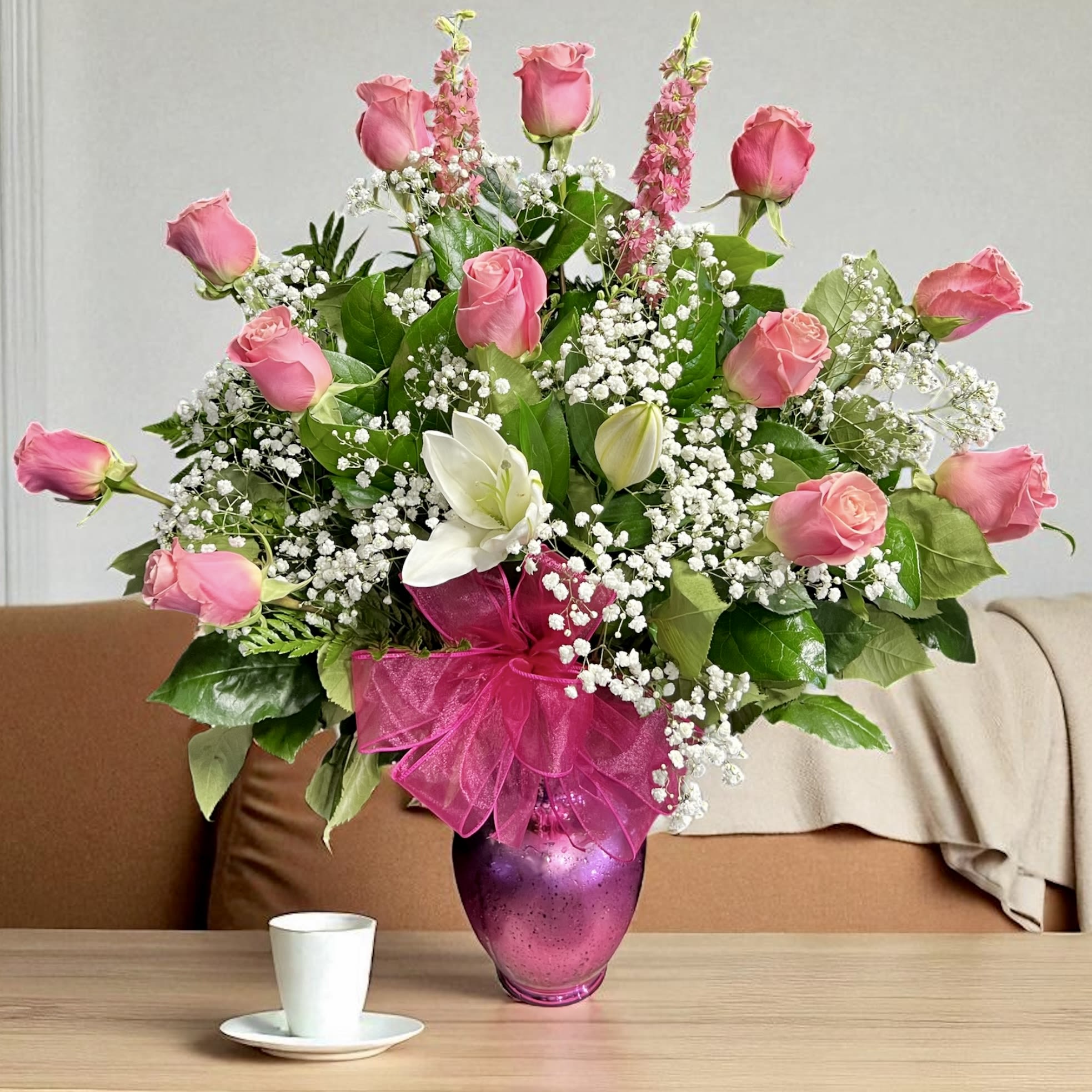 Tall arrangement of pink roses, white lilies, and baby’s-breath in a pink vase with a ribbon bow.
