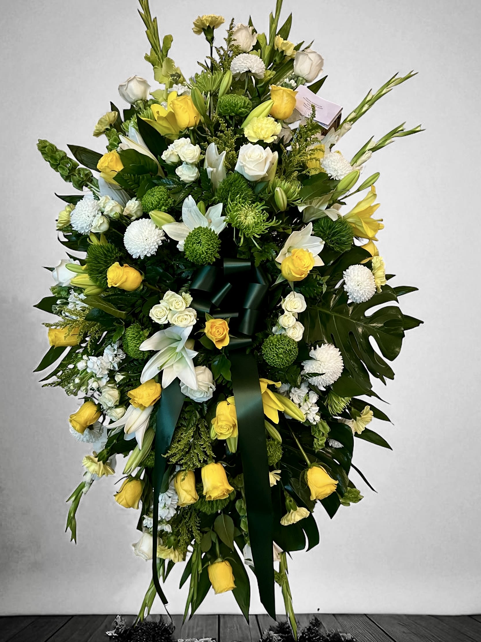 Tall yellow and white standing spray with roses, lilies, mums and dark green ribbon on an easel