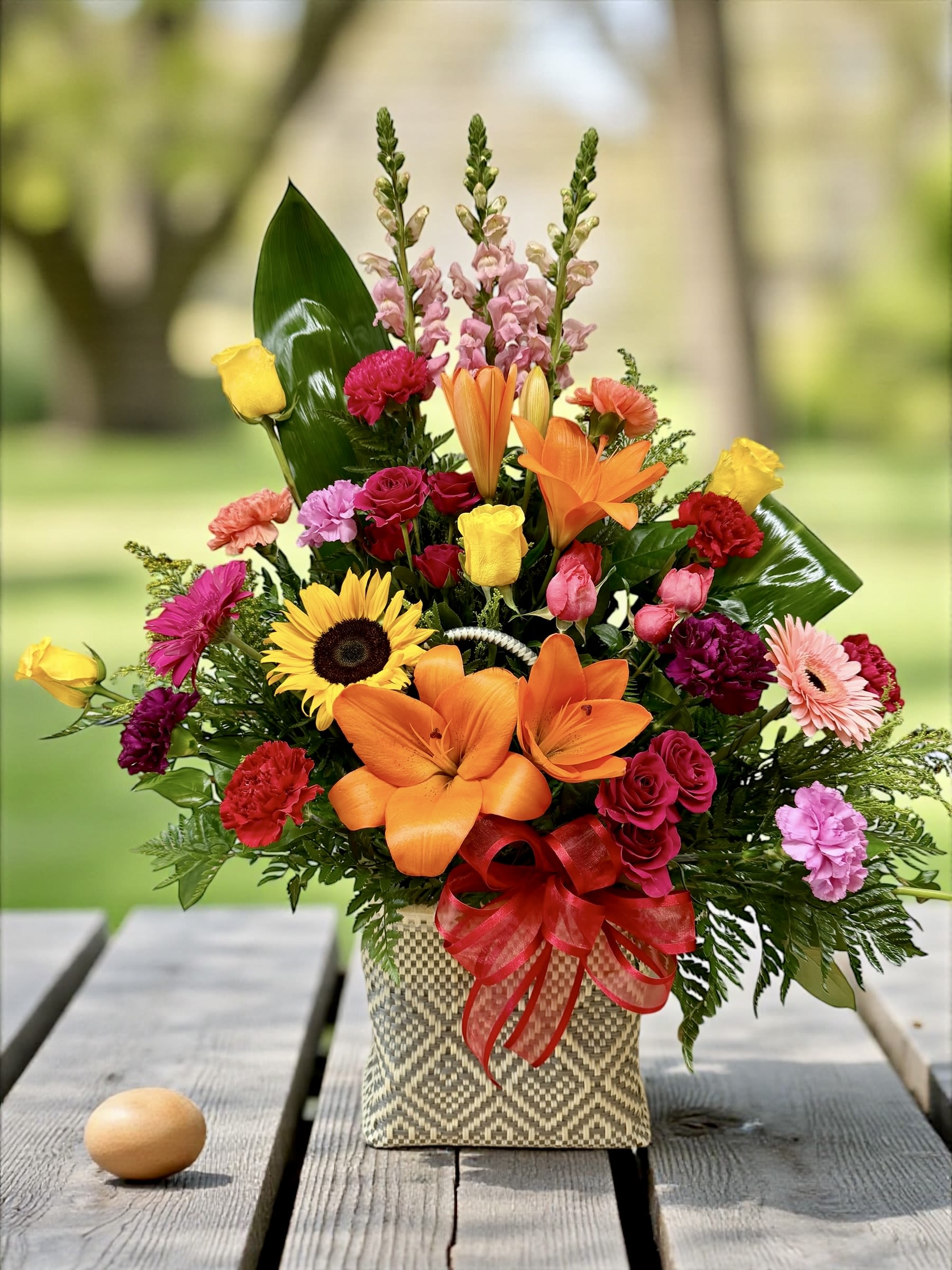 Colorful mixed flower arrangement in a woven basket with a red ribbon