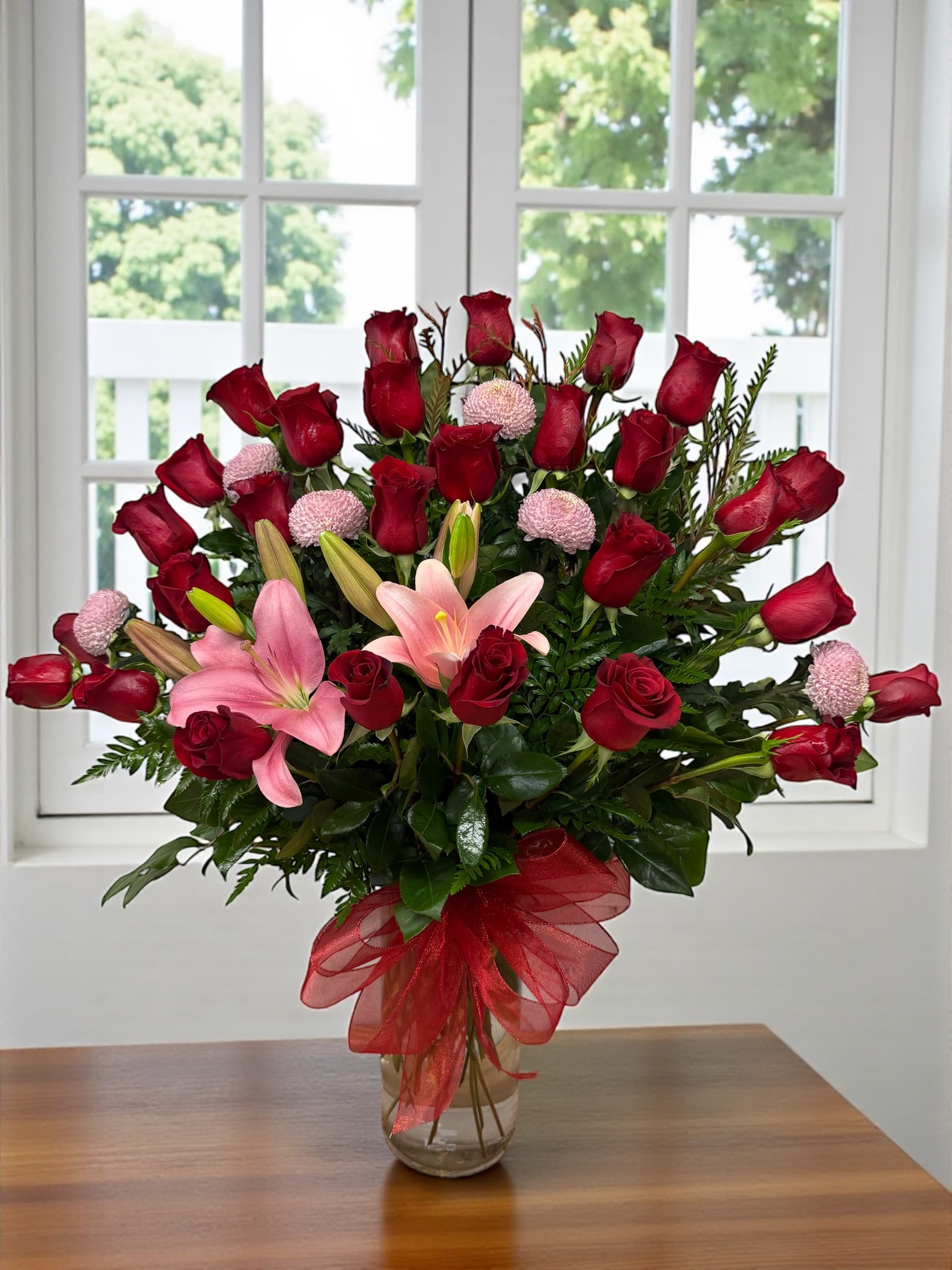 Bouquet of red roses and pink lilies in a glass vase with a red ribbon
