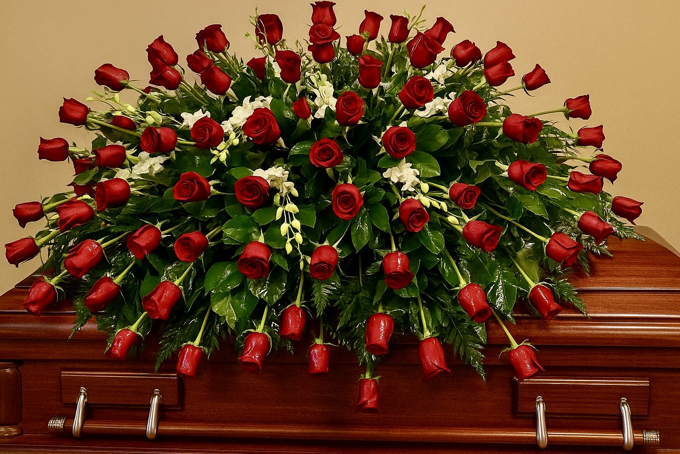 Red rose casket spray with white orchids arranged over a polished wood casket