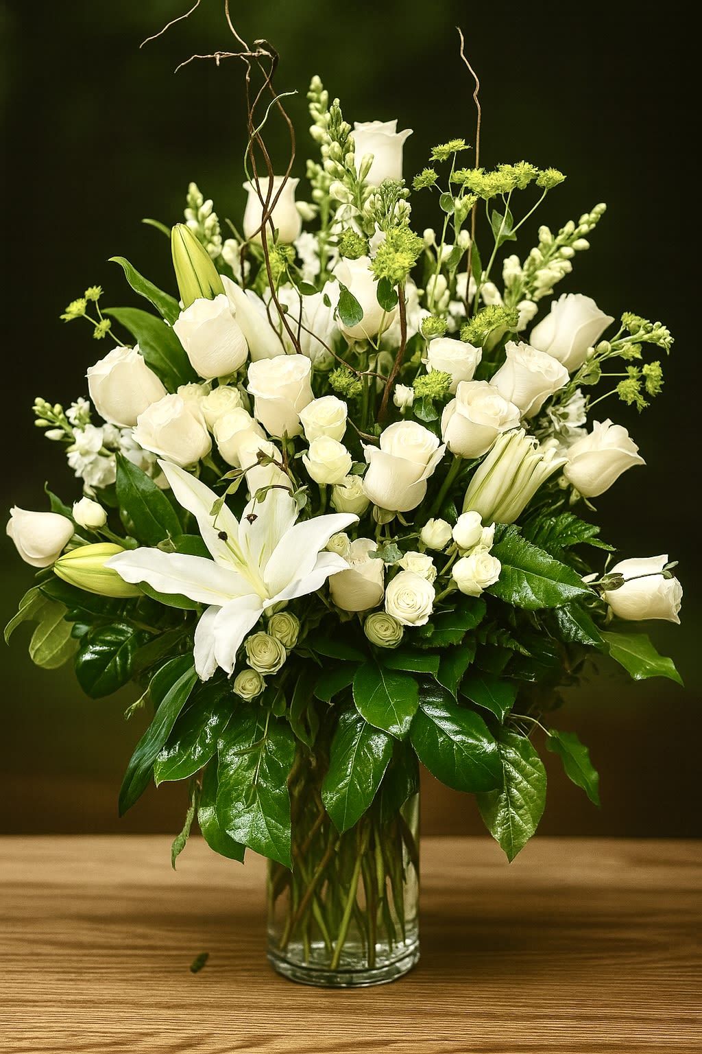 Tall arrangement of white roses and lilies with green accents in a clear glass vase