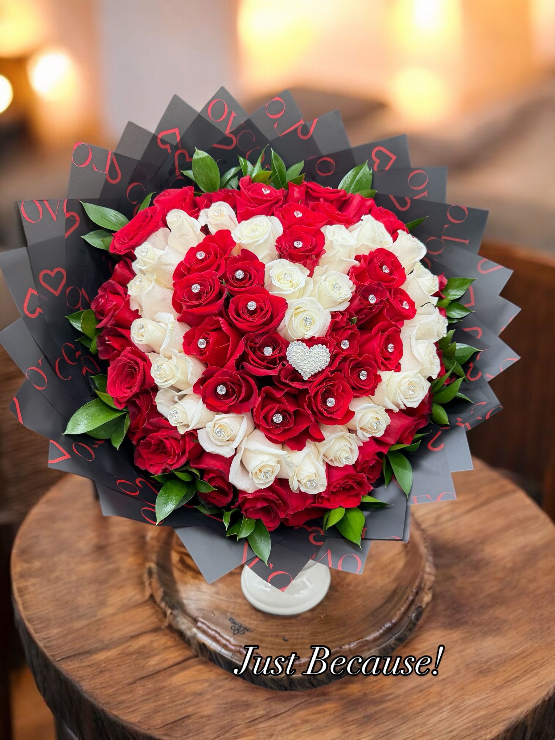 Red and white rose bouquet in black wrap with a white vase