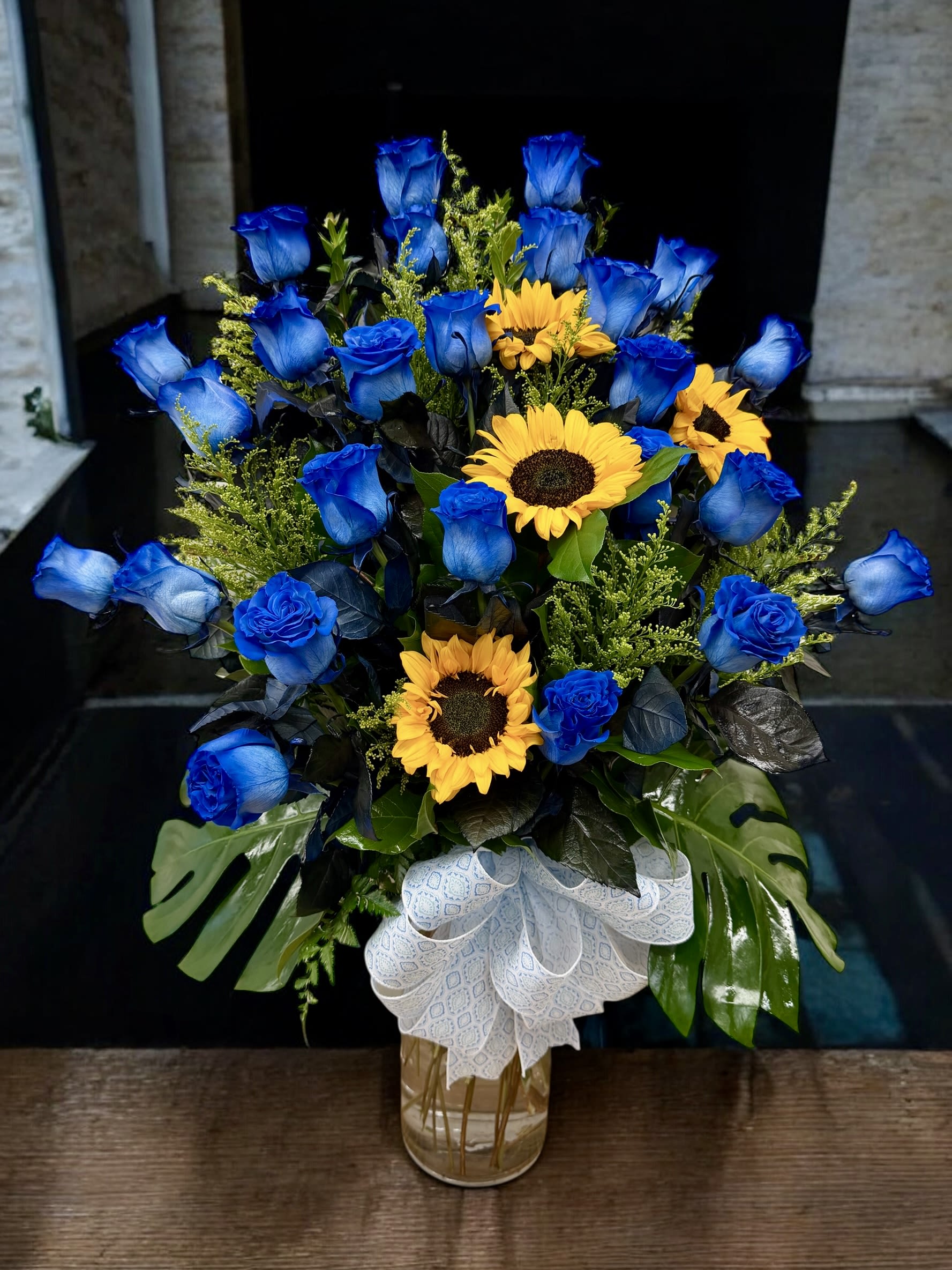 Blue roses and yellow sunflowers arranged in a glass vase