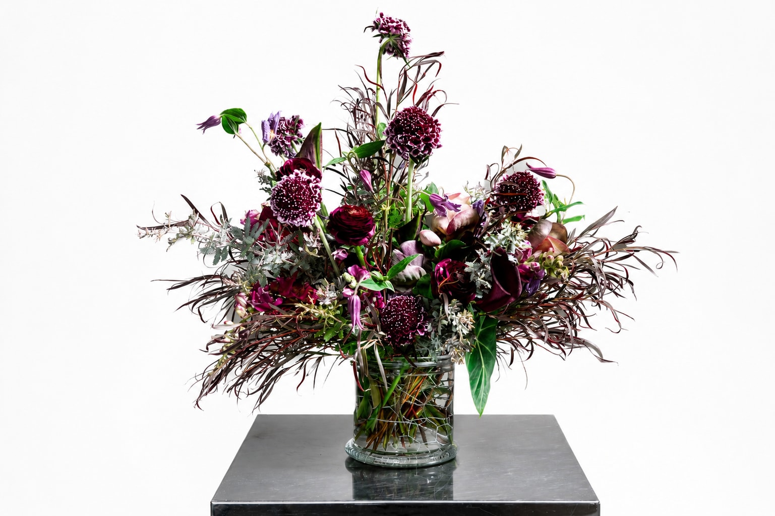 Tall burgundy and purple floral arrangement in a clear glass vase