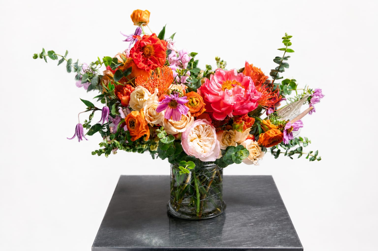 Mixed bouquet of orange, pink, and purple flowers in a glass vase