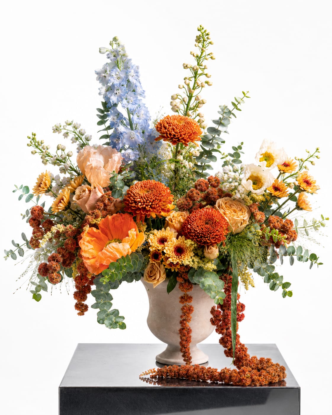 Large mixed floral arrangement in a beige vase with orange, blue, and cream blooms