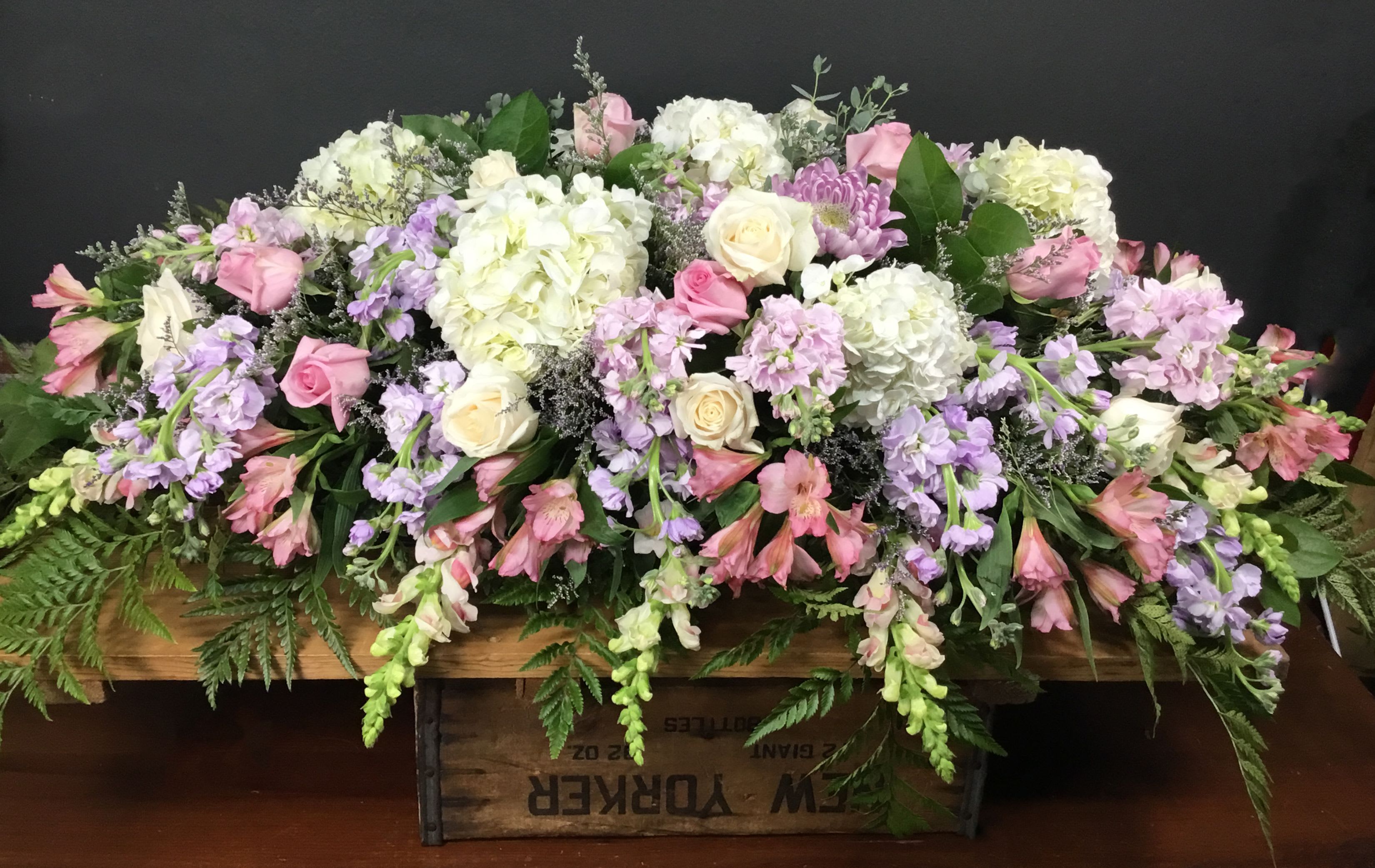Pink and Lavendar Casket Spray - Soft pastels nestle across this pink and lavender casket spray, a comforting sympathy arrangement designed to honor a life with gentle color and full, layered texture. The combination of pink roses and alstroemeria with lavender stock and cream roses creates a soothing, romantic palette that reads as both respectful and warmly personal for a funeral or memorial.