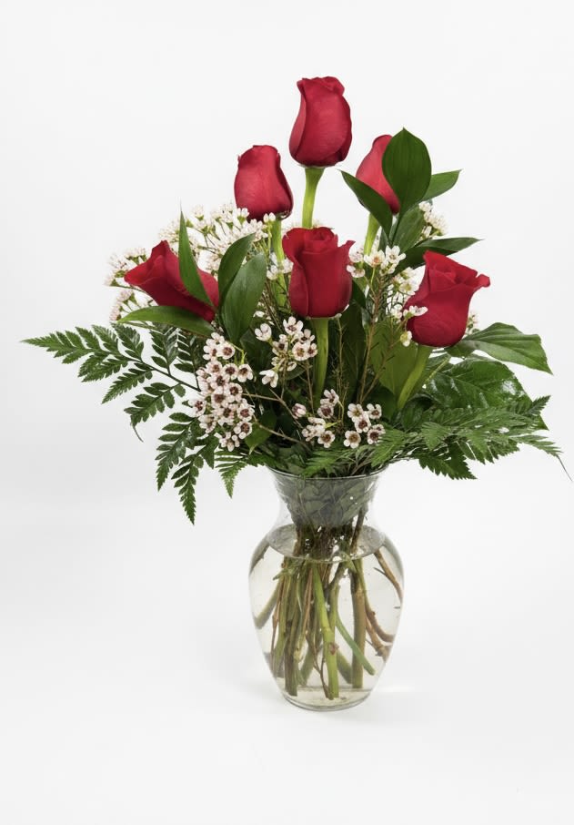 Red roses arranged in a clear glass vase with small white filler flowers