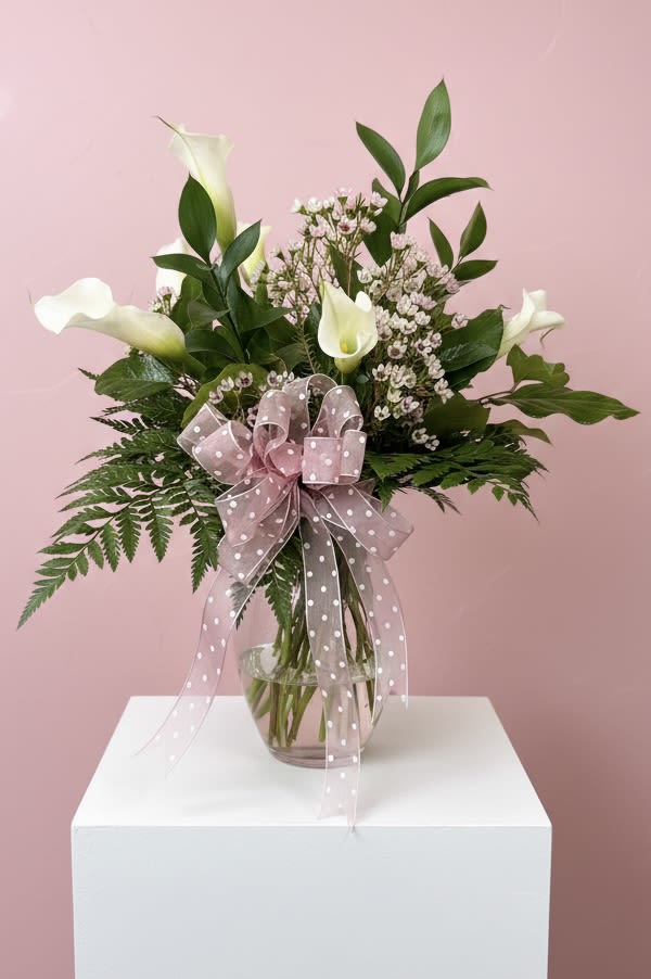 White calla lilies in a glass vase with a pink polka-dot bow