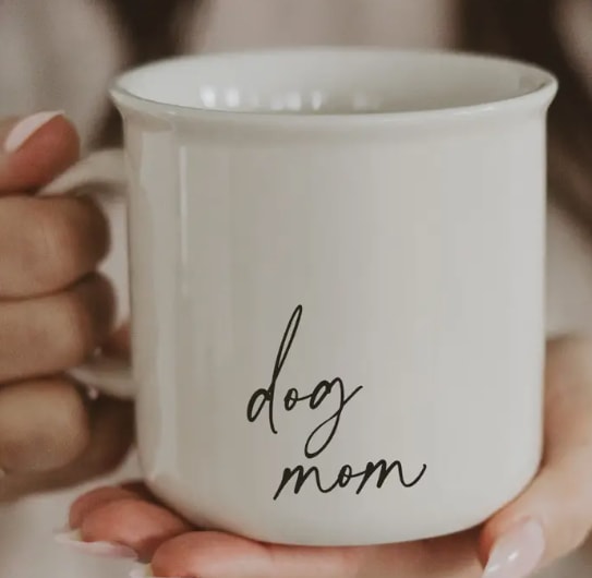 Dog Mom 11 oz Campfire Coffee Mug - Description Add a heartwarming touch to your collection with our Dog Mom Coffee Mug. Perfect for dog lovers, this thoughtful gift is ideal for retail, celebrating the bond between pets and their owners.  DETAILS:  • 11 oz Capacity • Campfire Style Mug • Cream neutral color with black script "dog mom" design on both sides   • Size: 3.75"W x 3.63"H (4.88" w/handle) • Designed in the USA, Imported 
