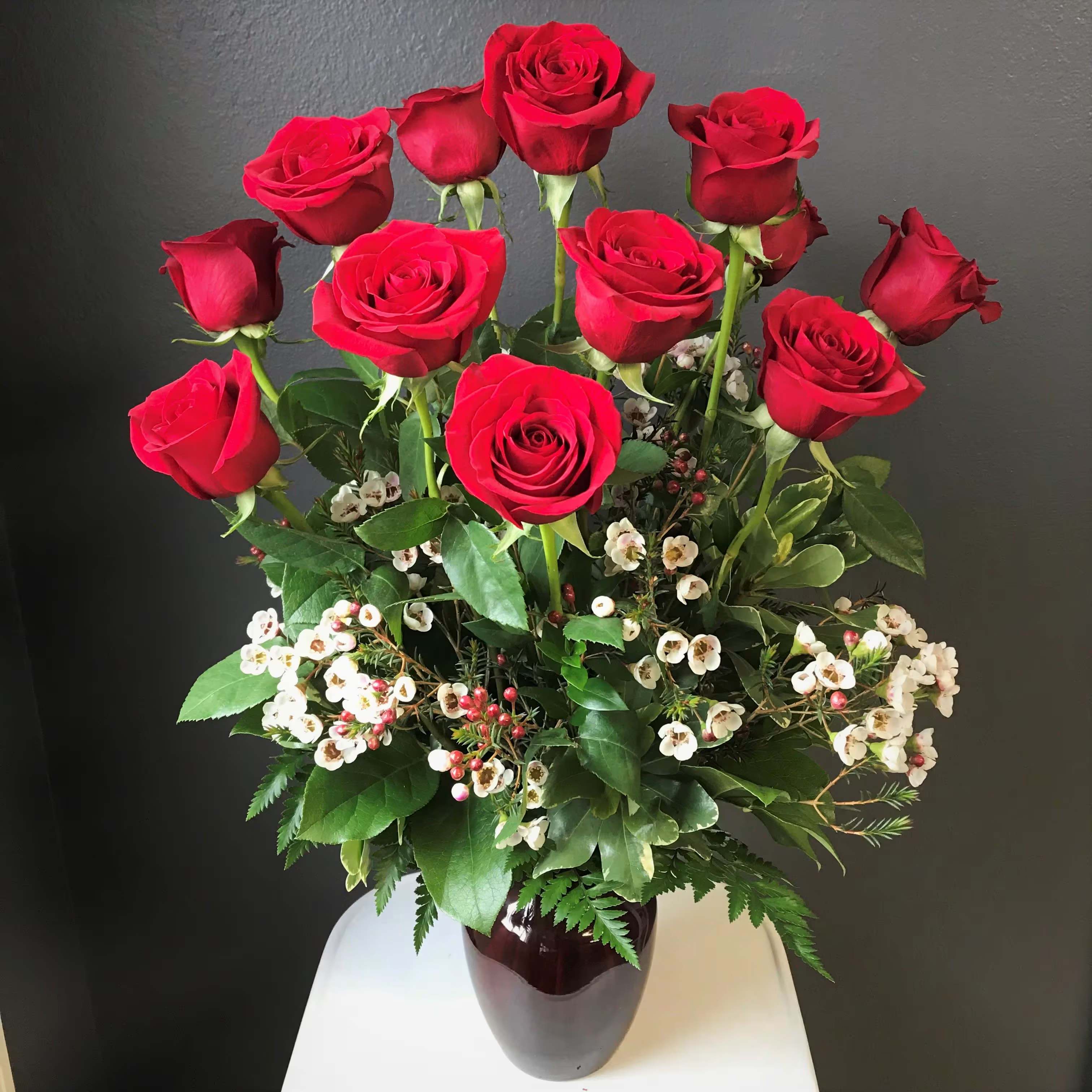 Red roses arranged in a dark vase with small white filler flowers